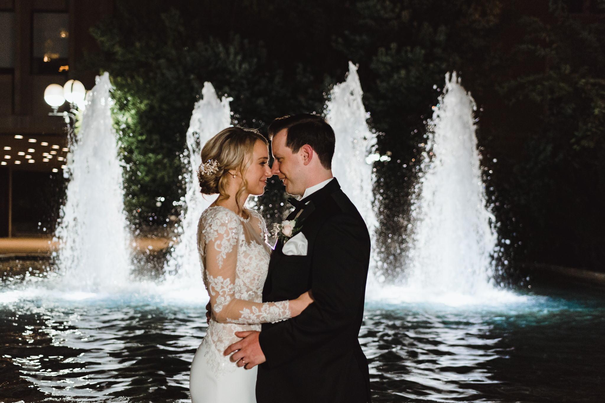bride and groom in a tight embrace in front of a water fountain with 4 columns of water shooting upwards behind them iconic downtown Toronto wedding photographer Gillian Foster