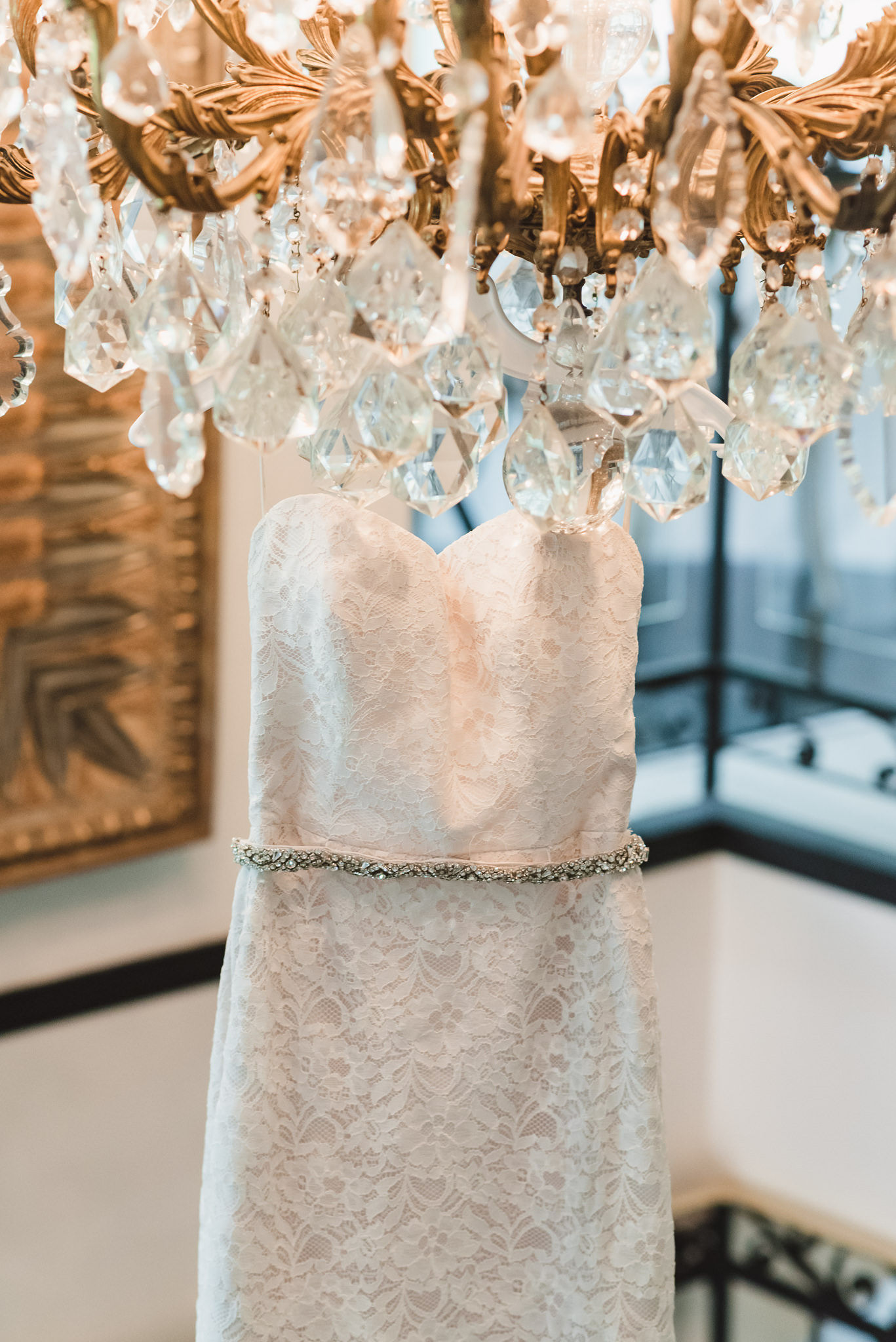 brides white wedding dress hanging from gold and crystal chandelier before Parisian inspired wedding at La Maquette in Toronto Ontario