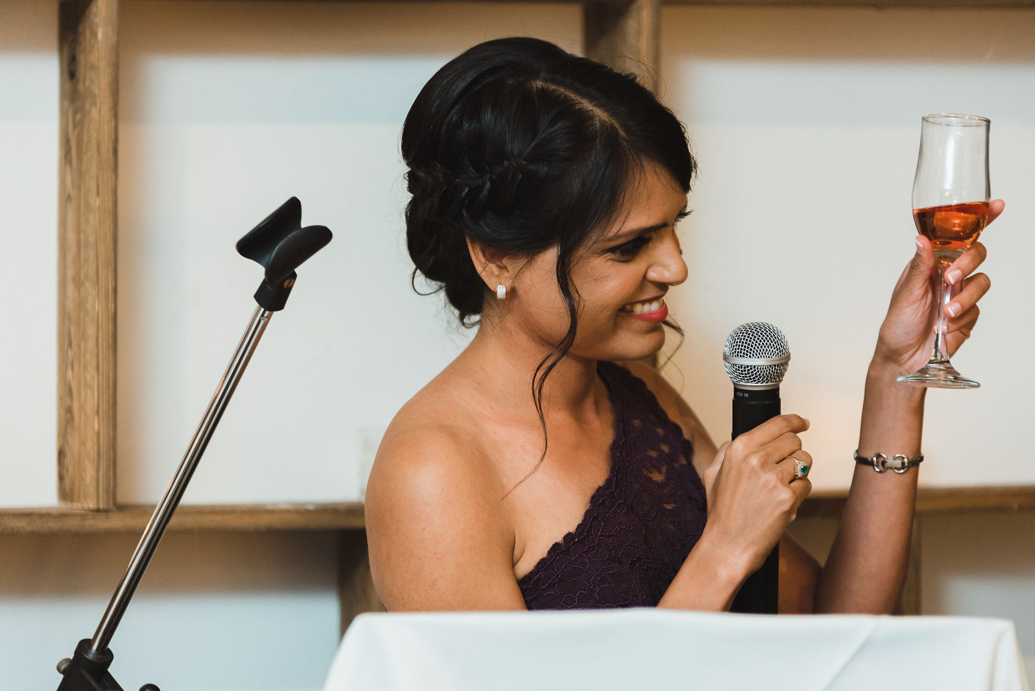 bridesmaid reading her speech into a microphone and toasting the bride and groom with a glass of wine during their Parisian inspired wedding at La Maquette in Toronto Ontario