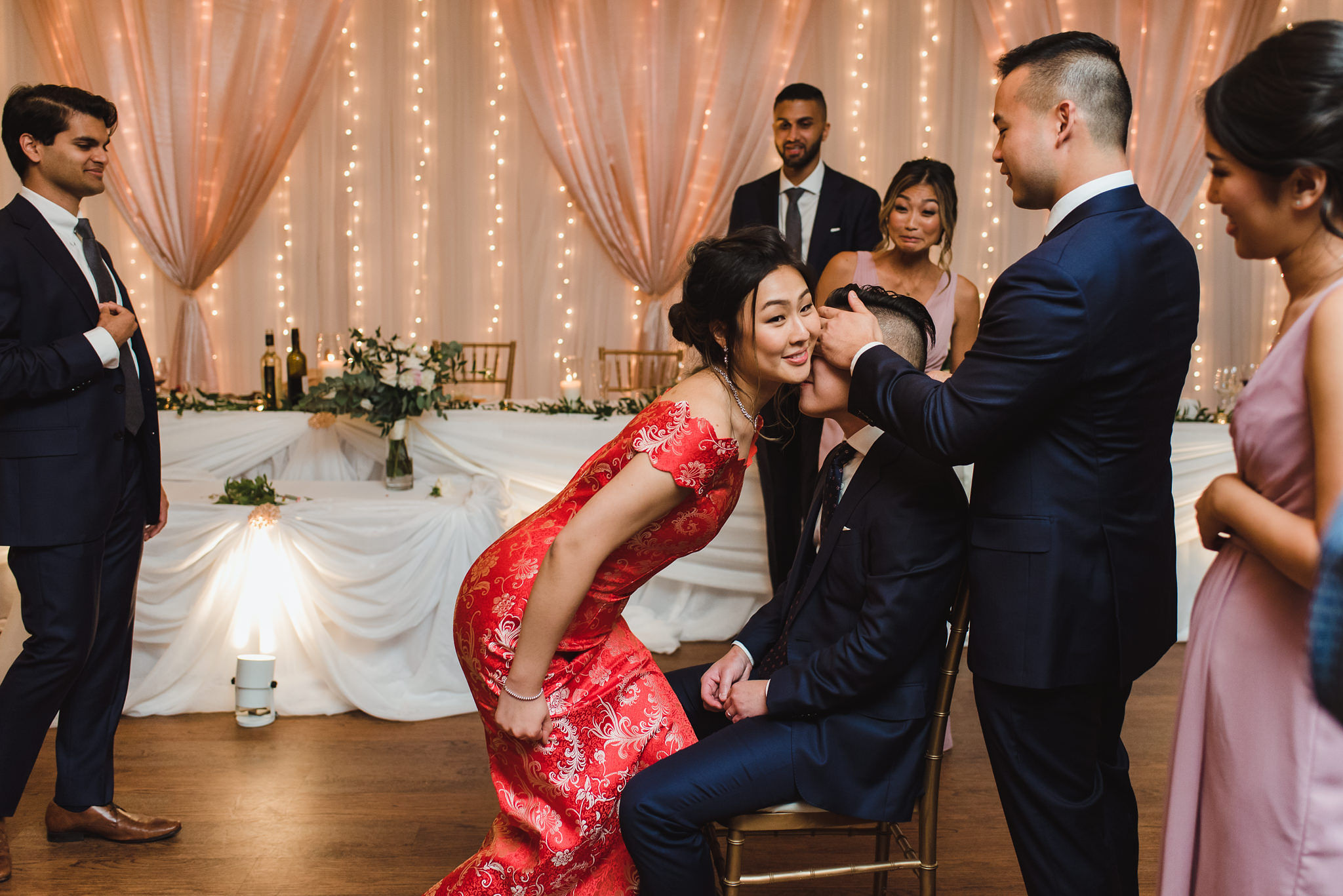 bride wearing red dress putting her cheek on groom while playing a wedding game at venue at Fantasy Farms in Toronto Ontario