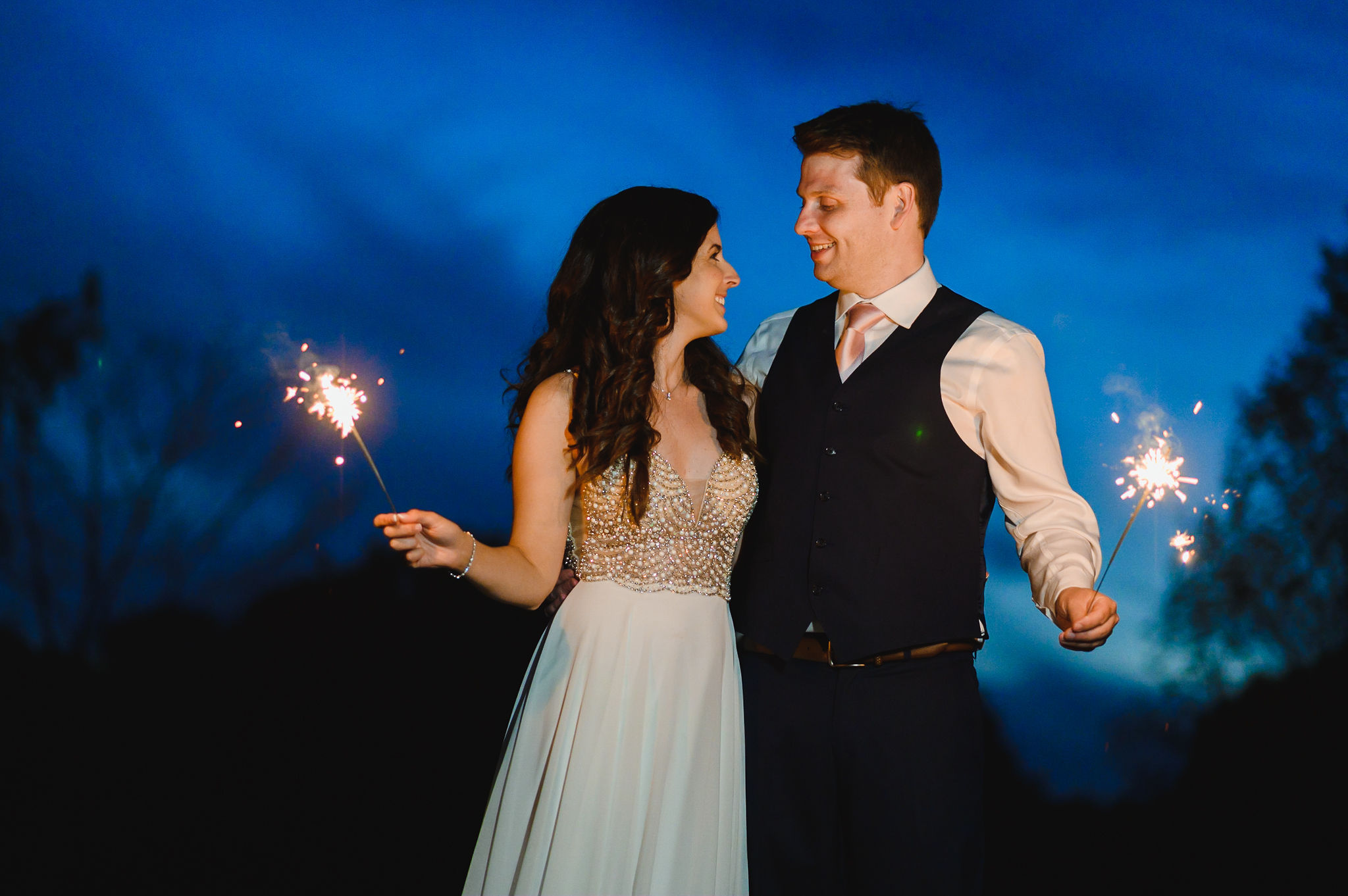 bride and groom standing with arms wrapped around each other and holding sparklers after their special wedding at the Royal Ashburn in Toronto