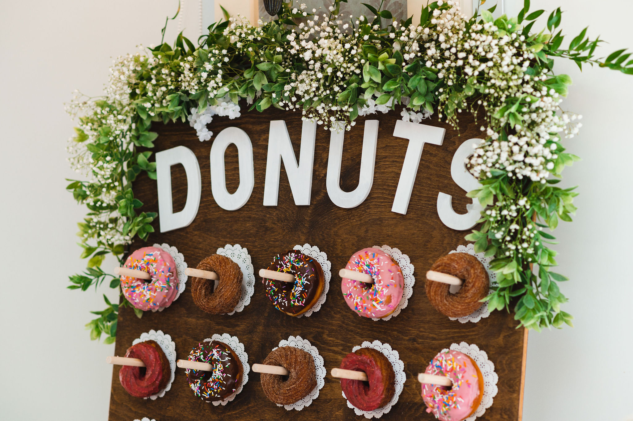 a wooden board with white flowers on top and the word "DONUTS" written across it in white with donuts hanging below on pegs Carver cottage wedding Pickering