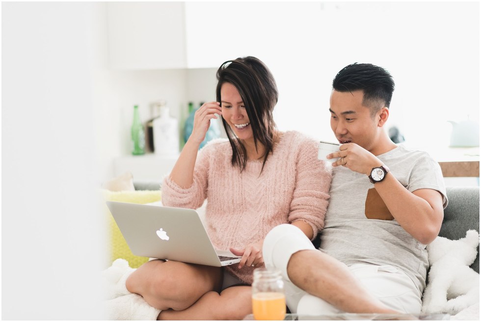 Couple sitting on the couch with a laptop, and drinking coffee. 