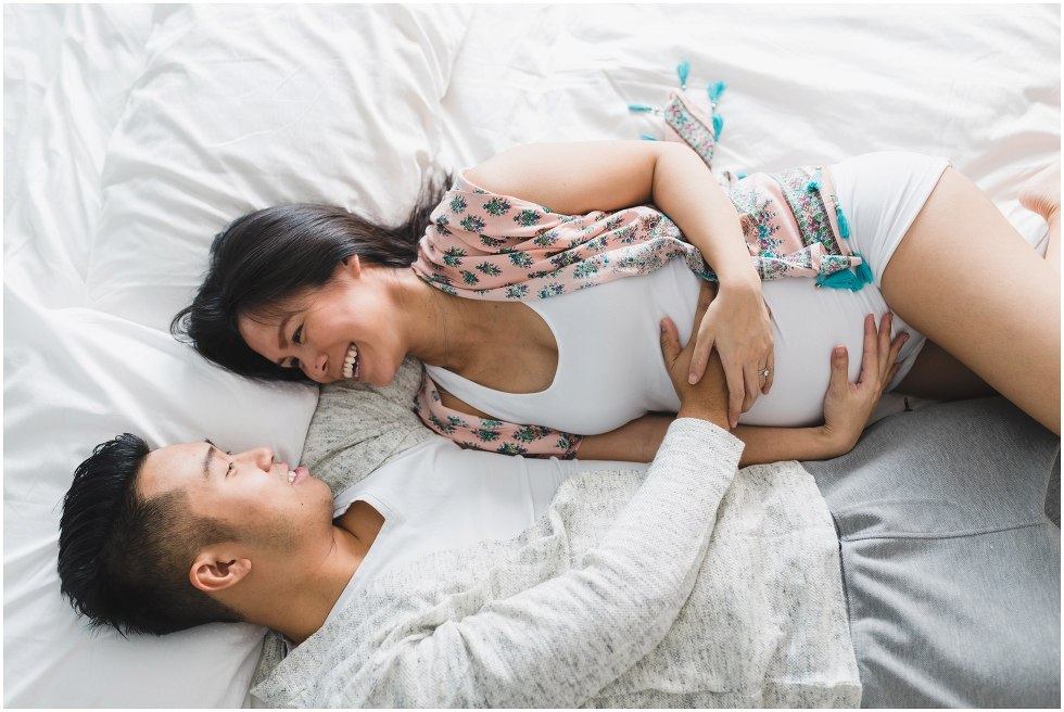 Parents to be cuddling up in bed, during their at home maternity session. 