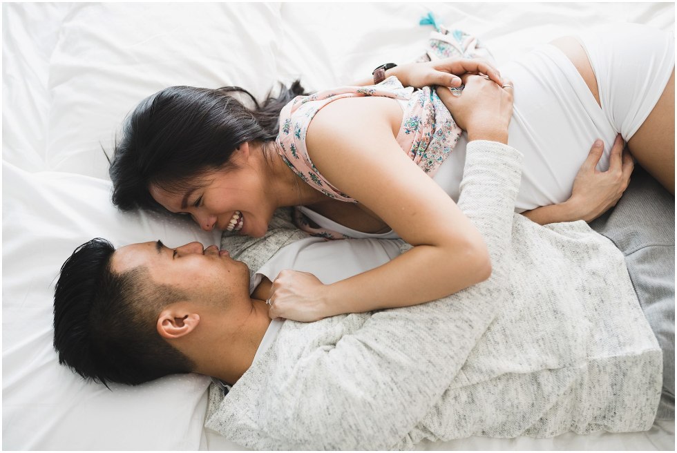 Husband and wife cuddle lovingly in bed during their at home maternity session. 