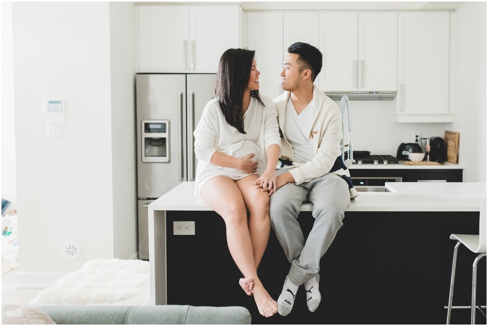 Married couple sitting on the kitchen counter, during their Toronto lifestyle maternity photos. 