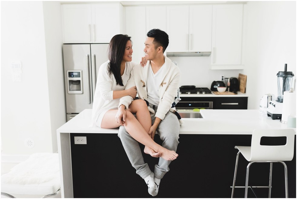 Couple sitting on kitchen counter, laughing and looking at each other. 