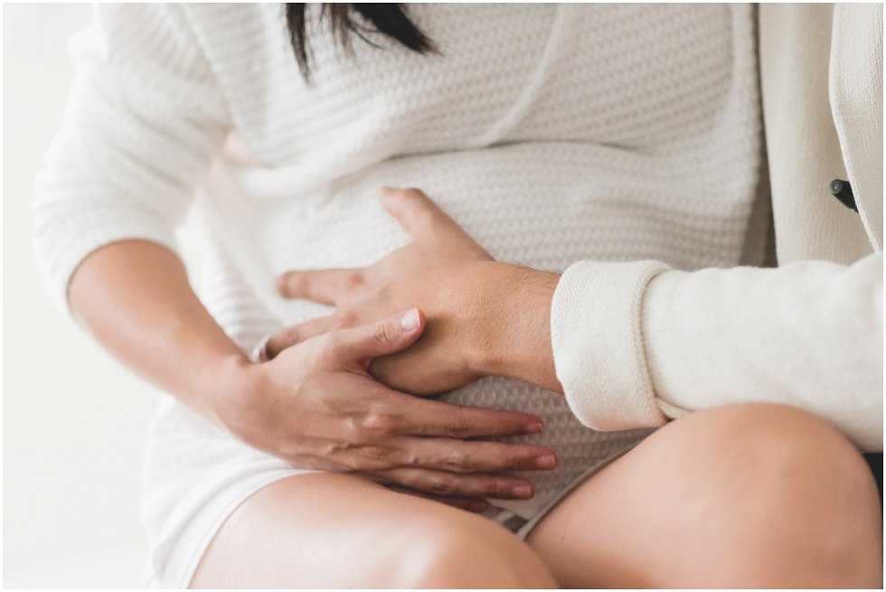 Couple feeling a baby bump, during their at home maternity session. 