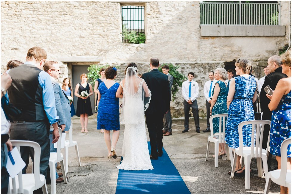 View of the brides dress from the back as her parents walk her down the isle 