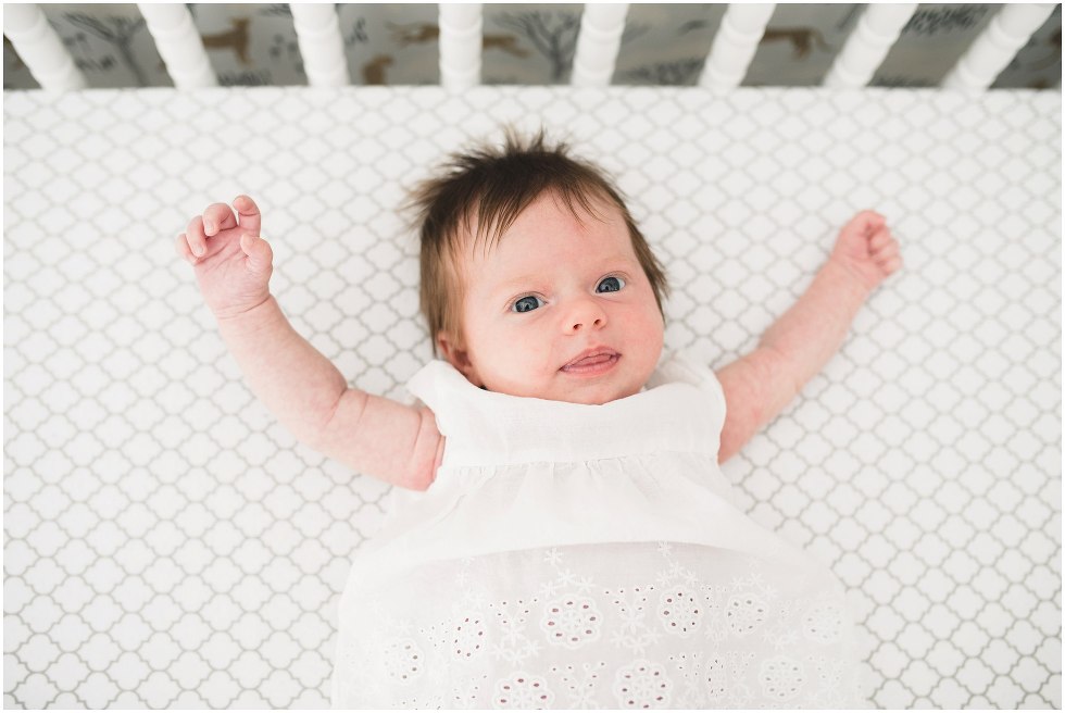 Newborn baby girl dressed in white waving her arms