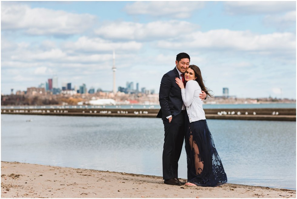 couple hugging on a beach with Toronto skyline in background proposal photographer Gillian Foster