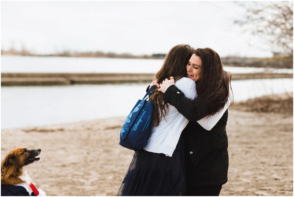 two women hugging on the beach with dog watching at their side Toronto proposal photography