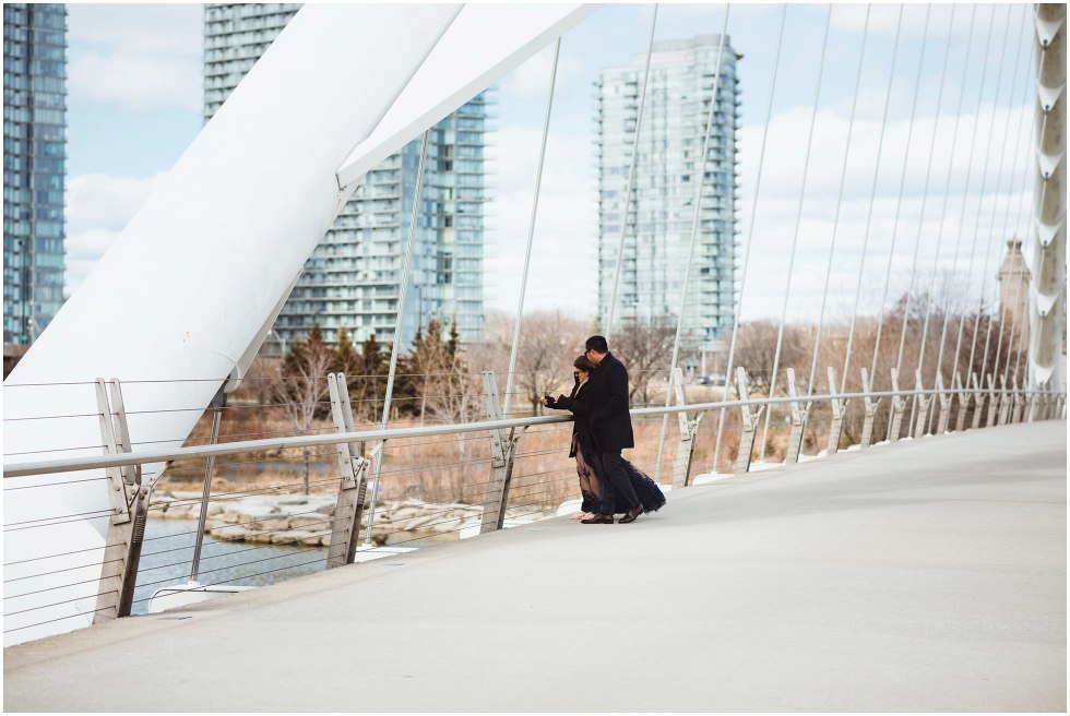 couple standing together on white bridge with condo buildings in background Toronto proposal photography