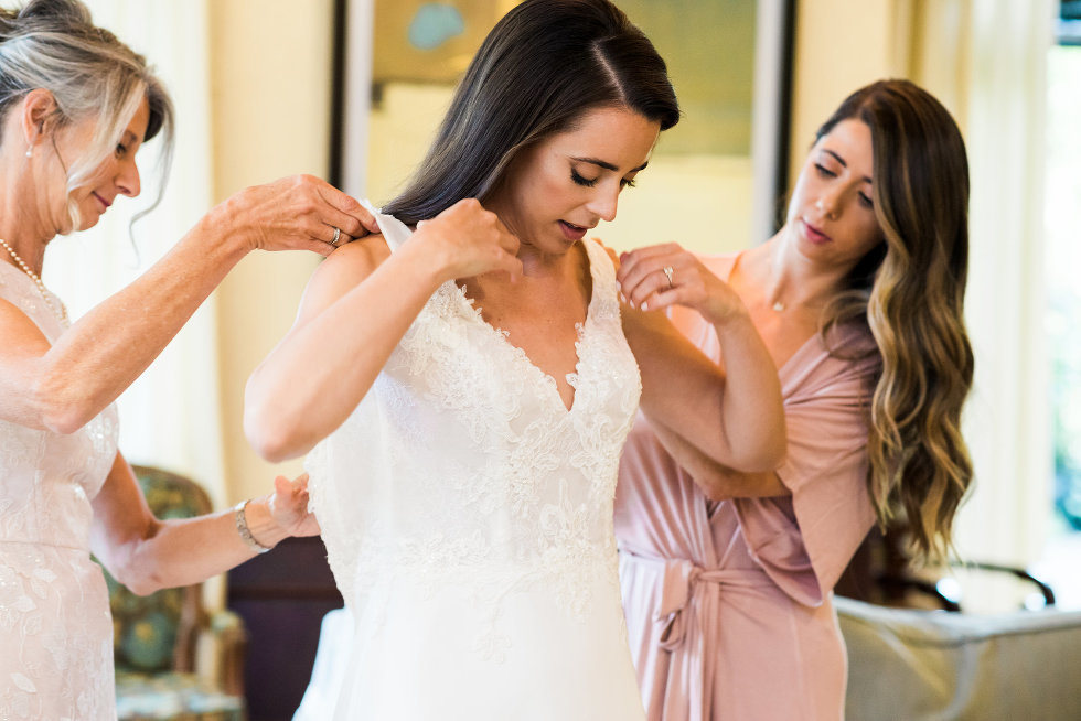 brides mother and bridesmaid helping bride into her dress Toronto wedding photographer