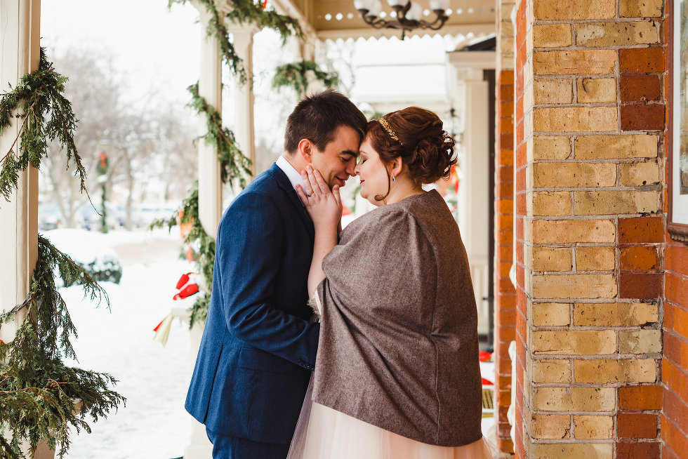 bride and groom embrace each other between white columns and brick wall Niagara wedding photography Gillian Foster