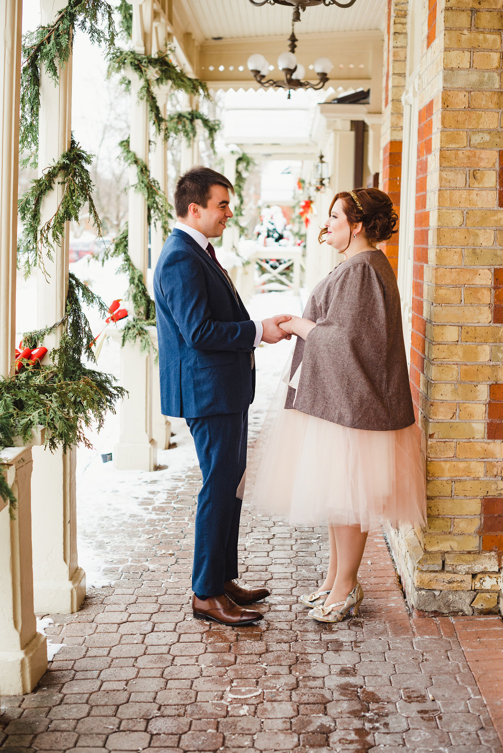 bride and groom hold hands between white columns and brick wall Niagara wedding photography Gillian Foster