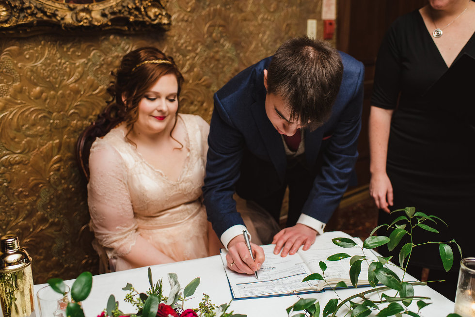 groom signs wedding certificate with bride watching Niagara wedding photography 