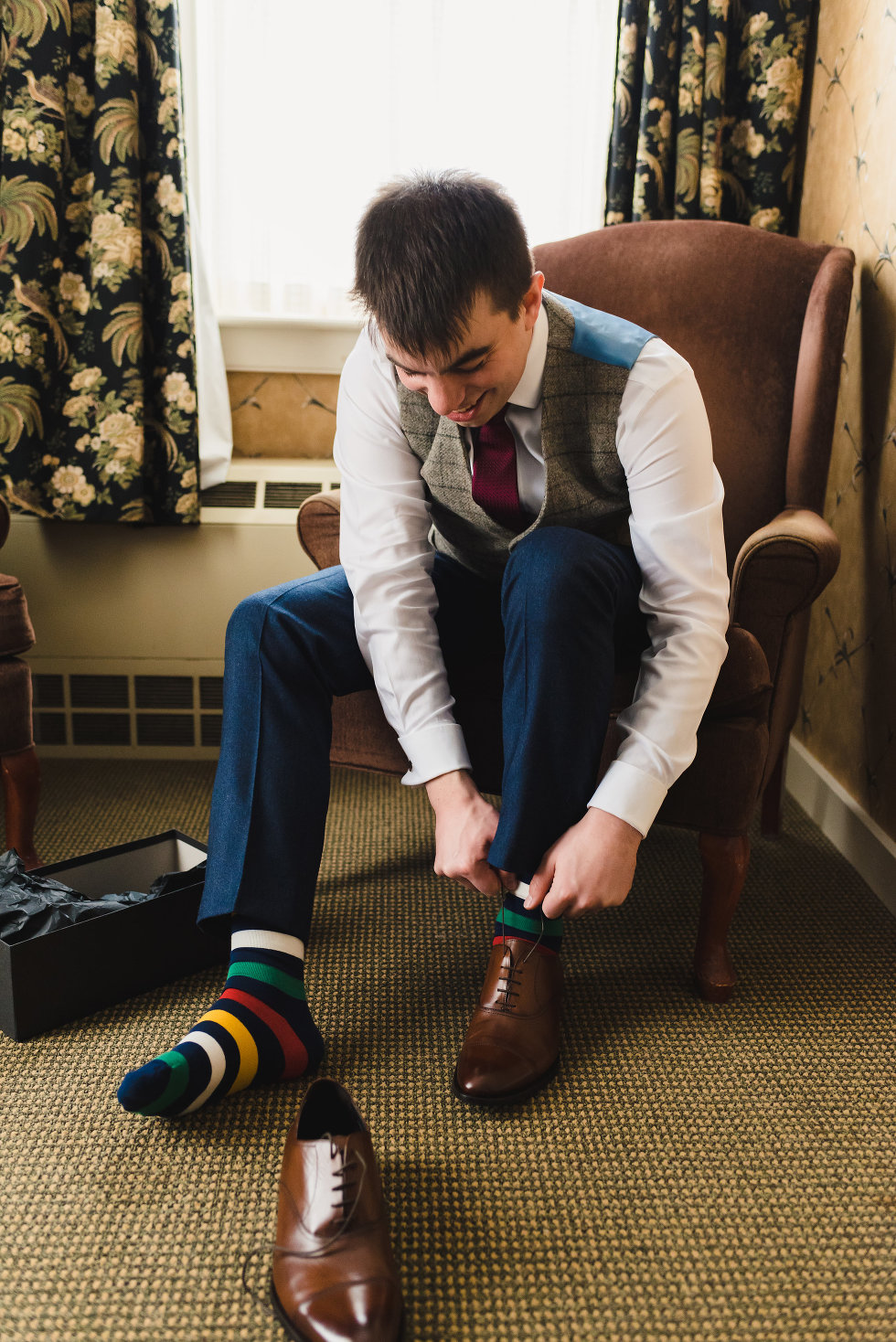 groom seated in chair tying up brown dress shoe with colourful striped socks Toronto wedding photography