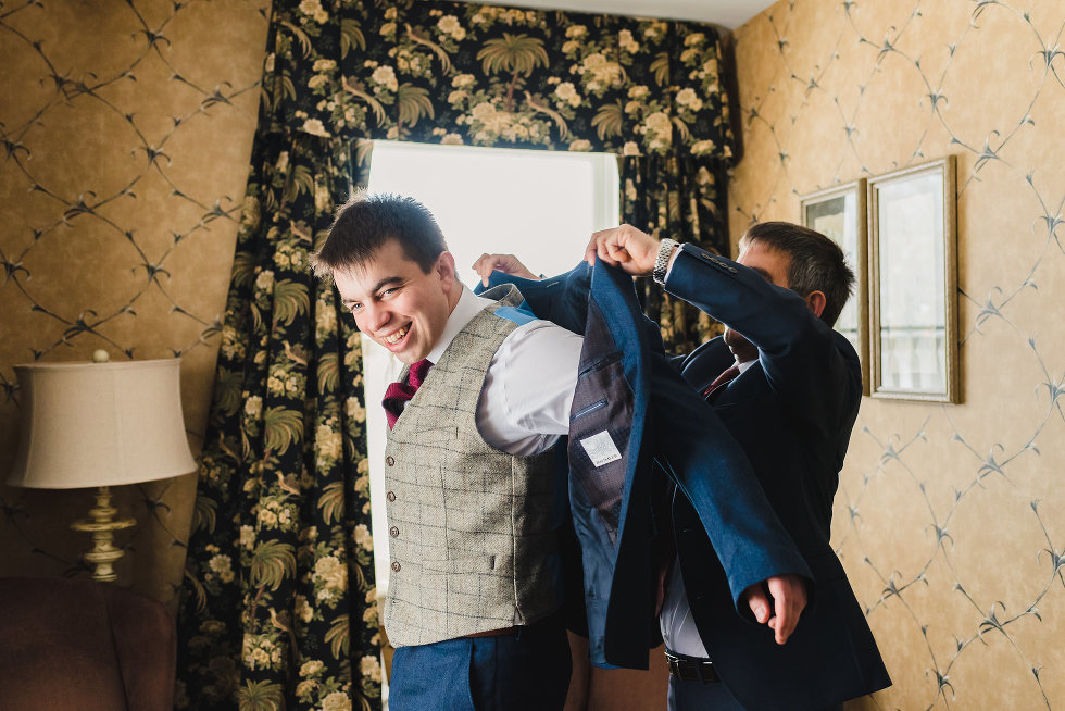 father of groom helping groom put on his blue suit jacket Niagara wedding photographer