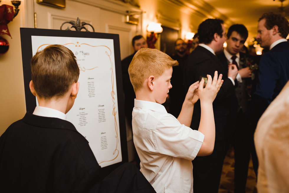 a couple of kids inspecting the seating chart for the reception while the other boy takes pictures Prince of Wales Hotel Niagara wedding photography