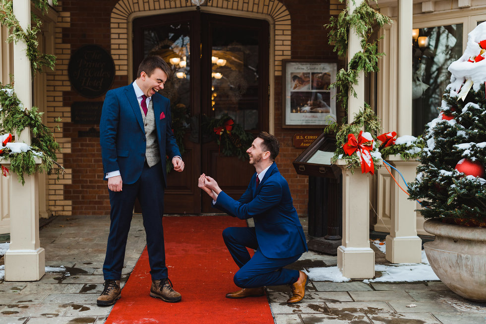 groomsman on one knee pretending to propose to a laughing groom Prince of Wales Hotel Niagara wedding photography Gillian Foster