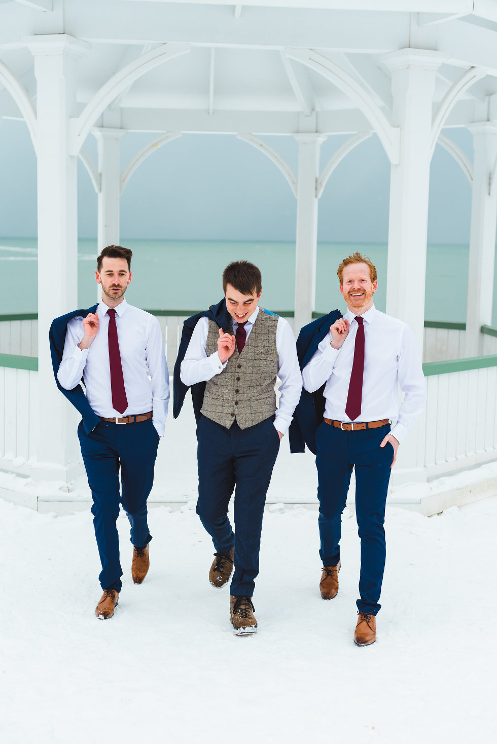 groom and his groomsmen walking away from white gazebo with their suit jackets hanging over their shoulders Prince of Wales Hotel Niagara wedding photography Gillian Foster