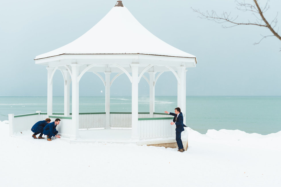 groom throwing snowball throw white gazebo at groomsmen hiding on other side Niagara wedding photography