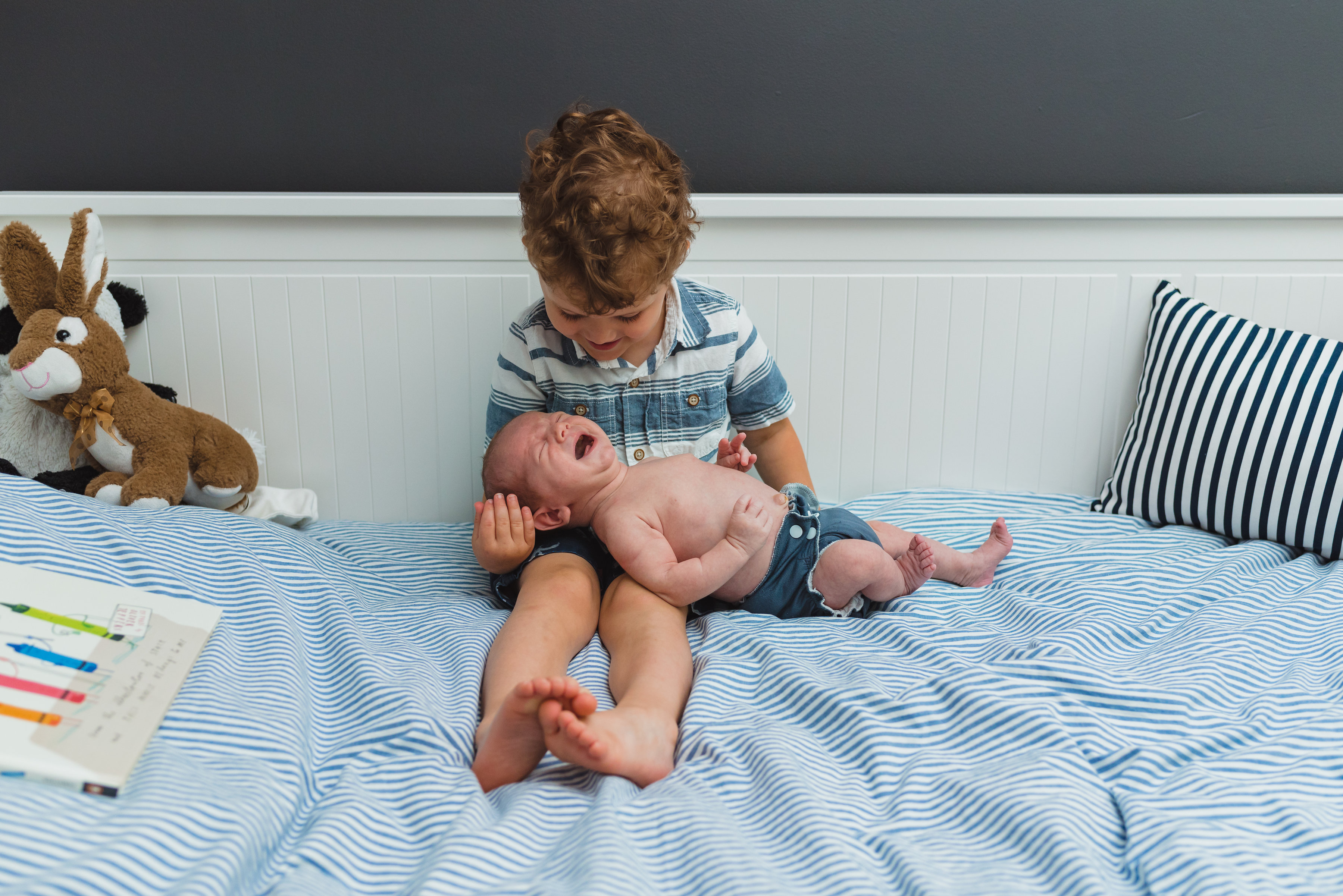 toddler sitting in his bed holding baby brother for newborn photo session toddler sitting in his bed holding baby brother for newborn photo session