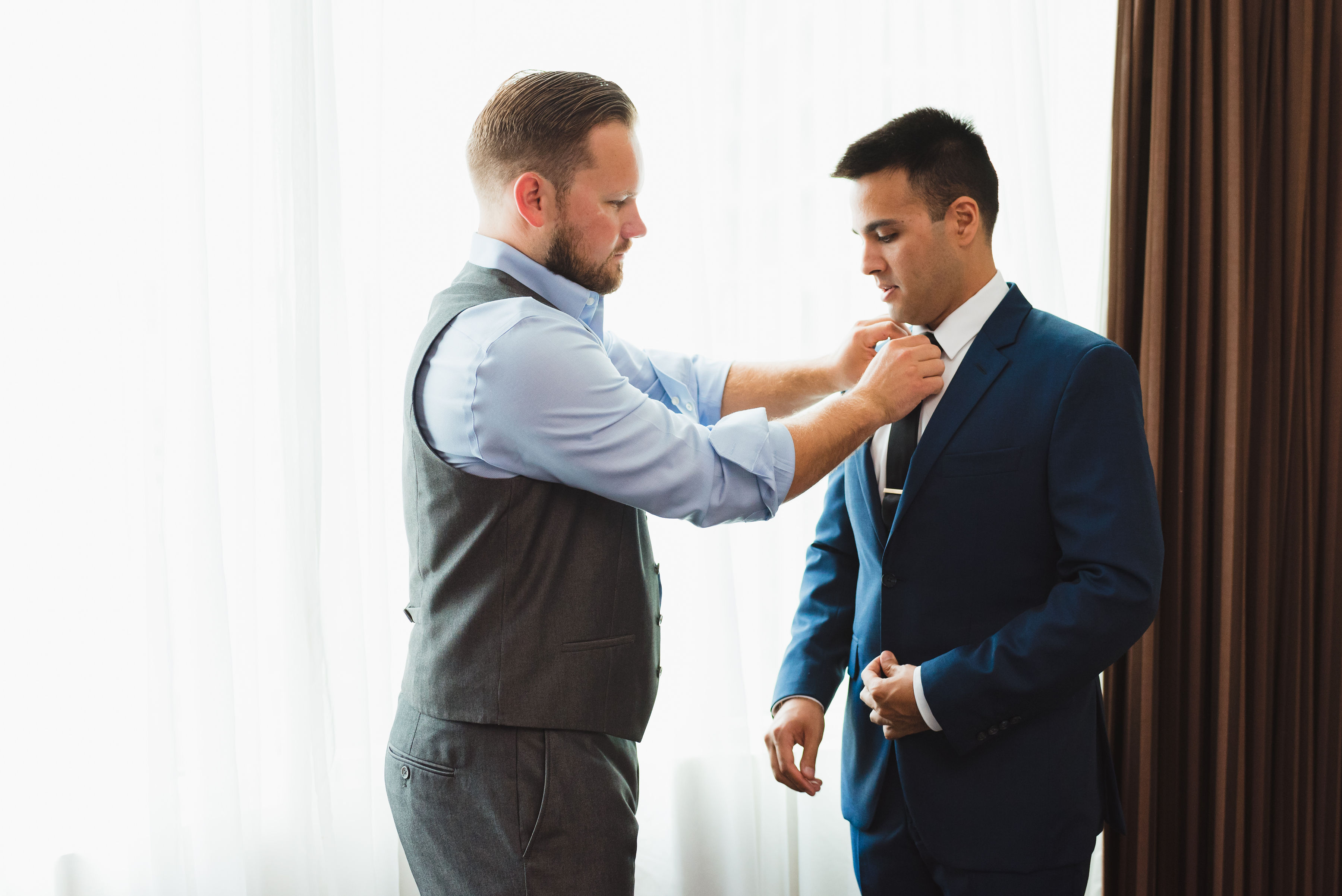 groomsman helping tighten grooms black neck tie Toronto brewery wedding photography