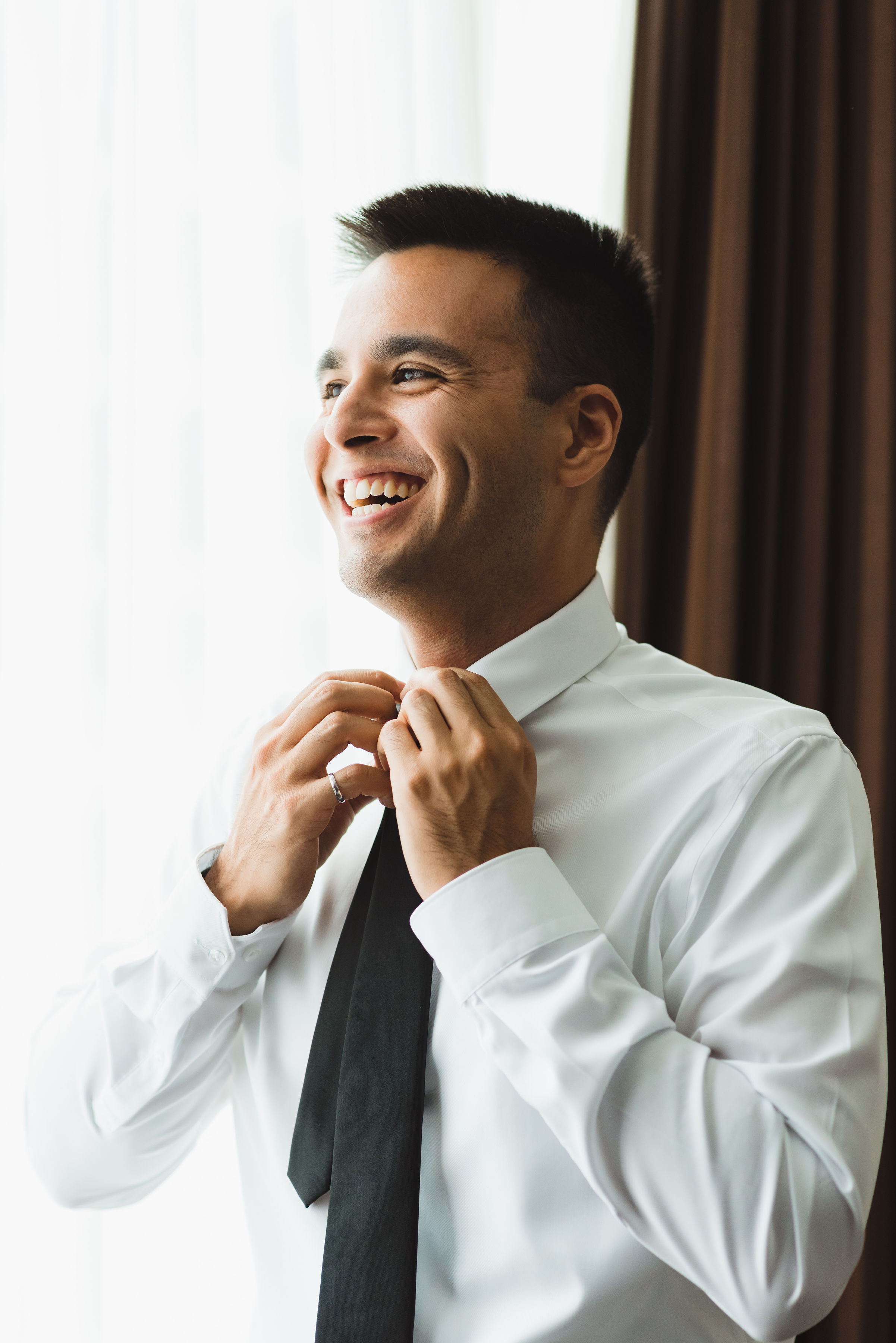 groom smiling while tying his black neck tie Toronto brewery wedding photography
