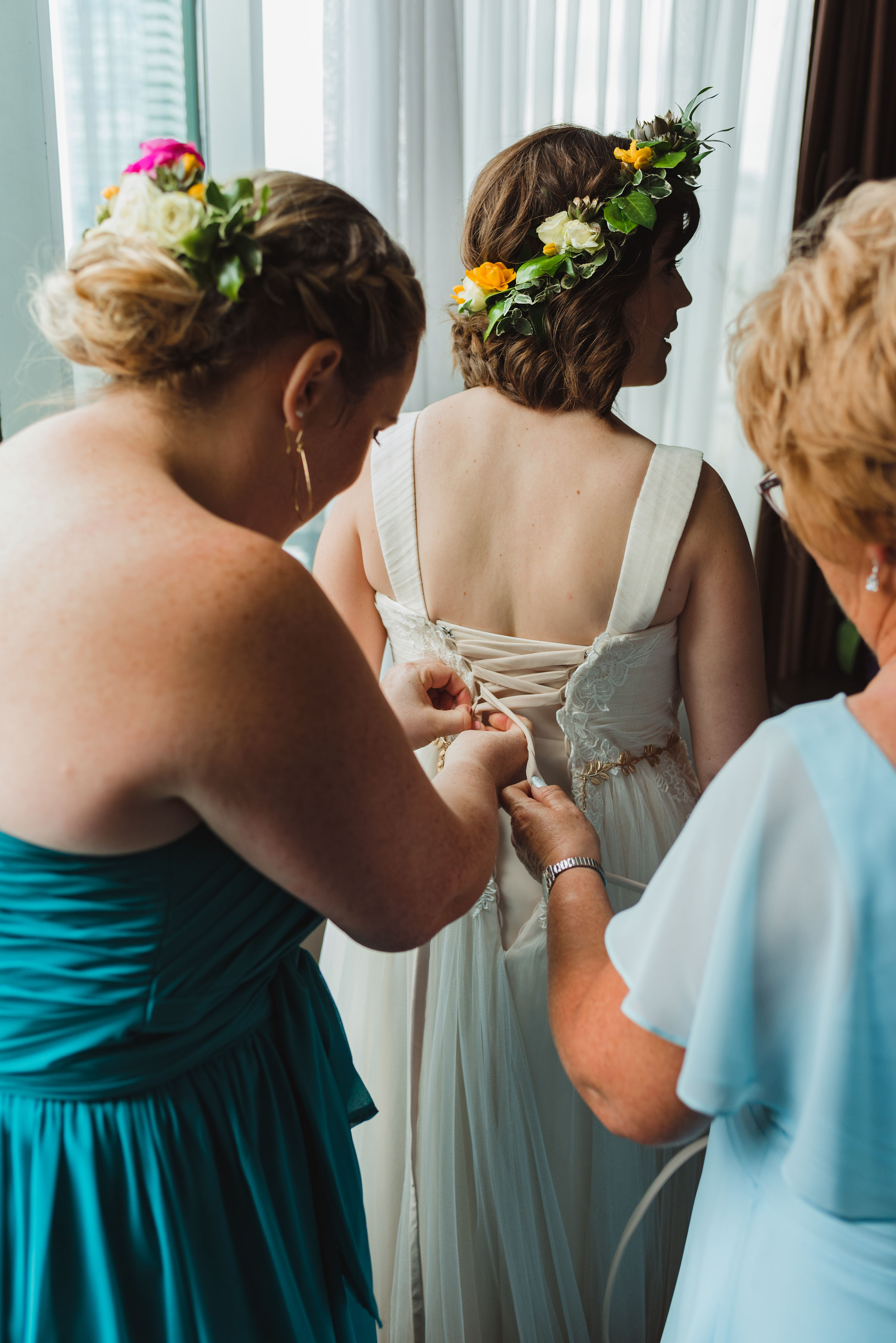 bride wearing flower crown having her gown tied up in the back by bridesmaid and mother Toronto Junction Craft Brewing wedding photography
