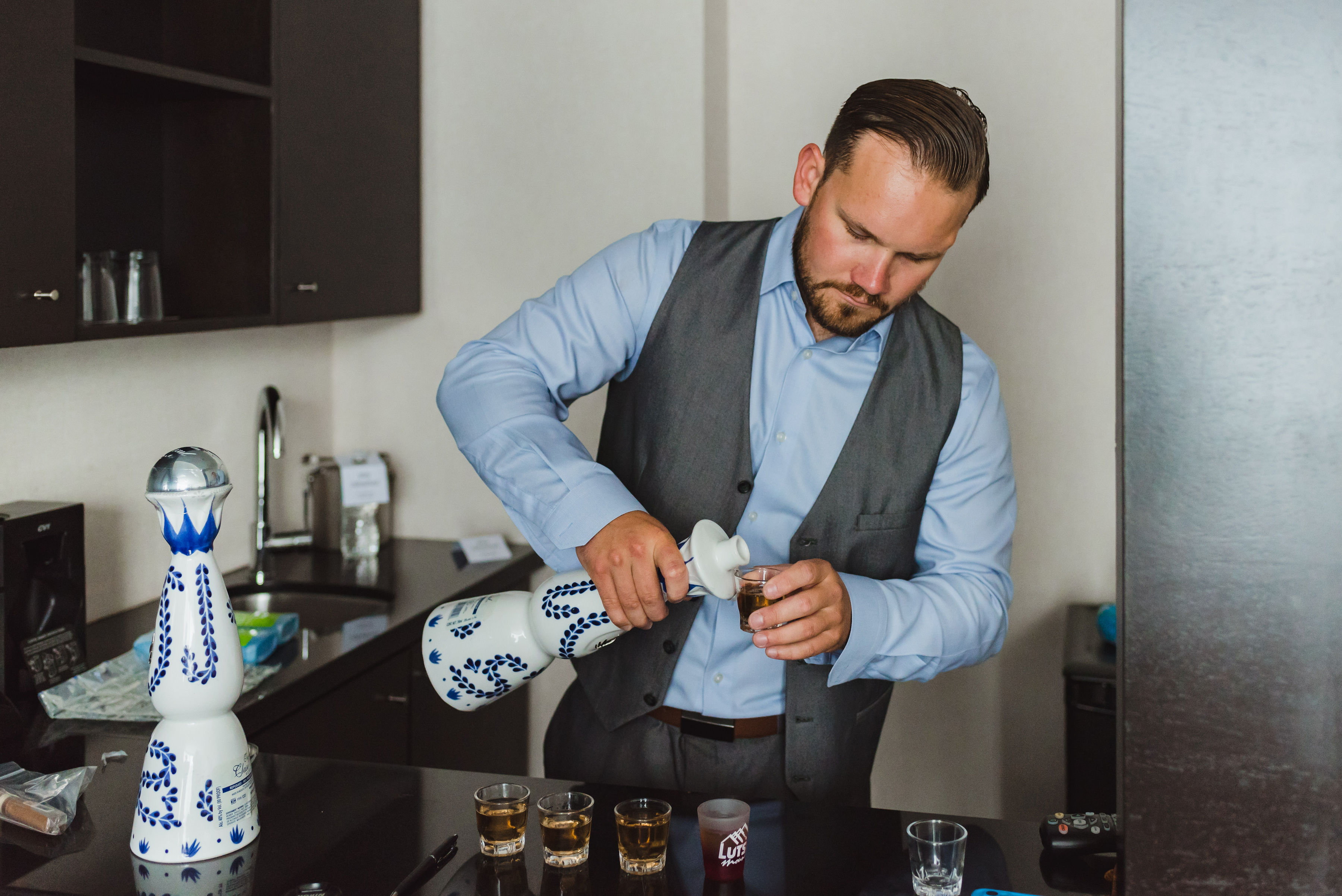 groomsman in blue dress shirt and grey vest pouring shots into 5 glasses Toronto Junction Craft Brewing photography