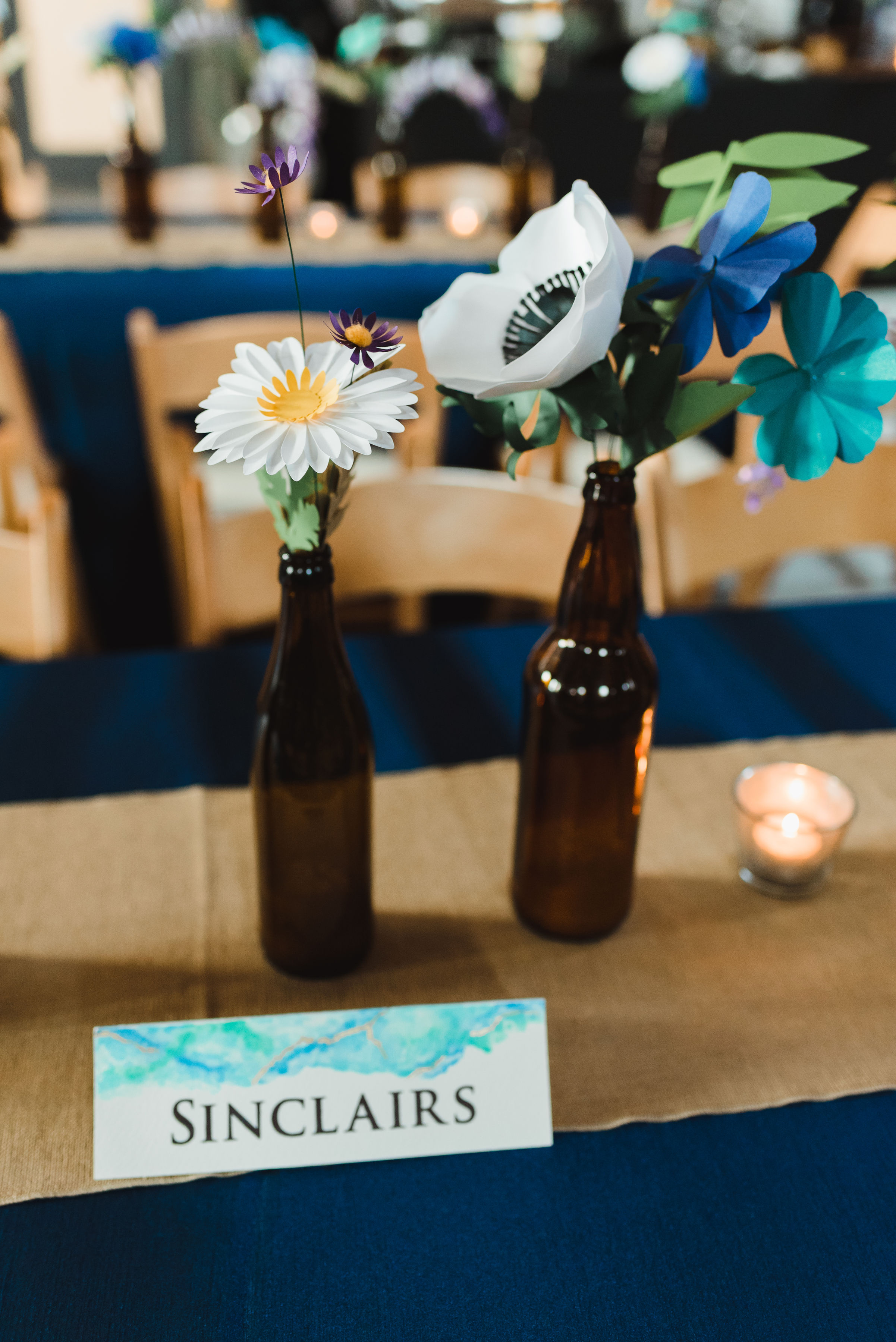 brown beer bottles with flowers placed in them on wedding reception table with a card reading "Sinclairs" in front of them Toronto Junction Craft Brewing wedding