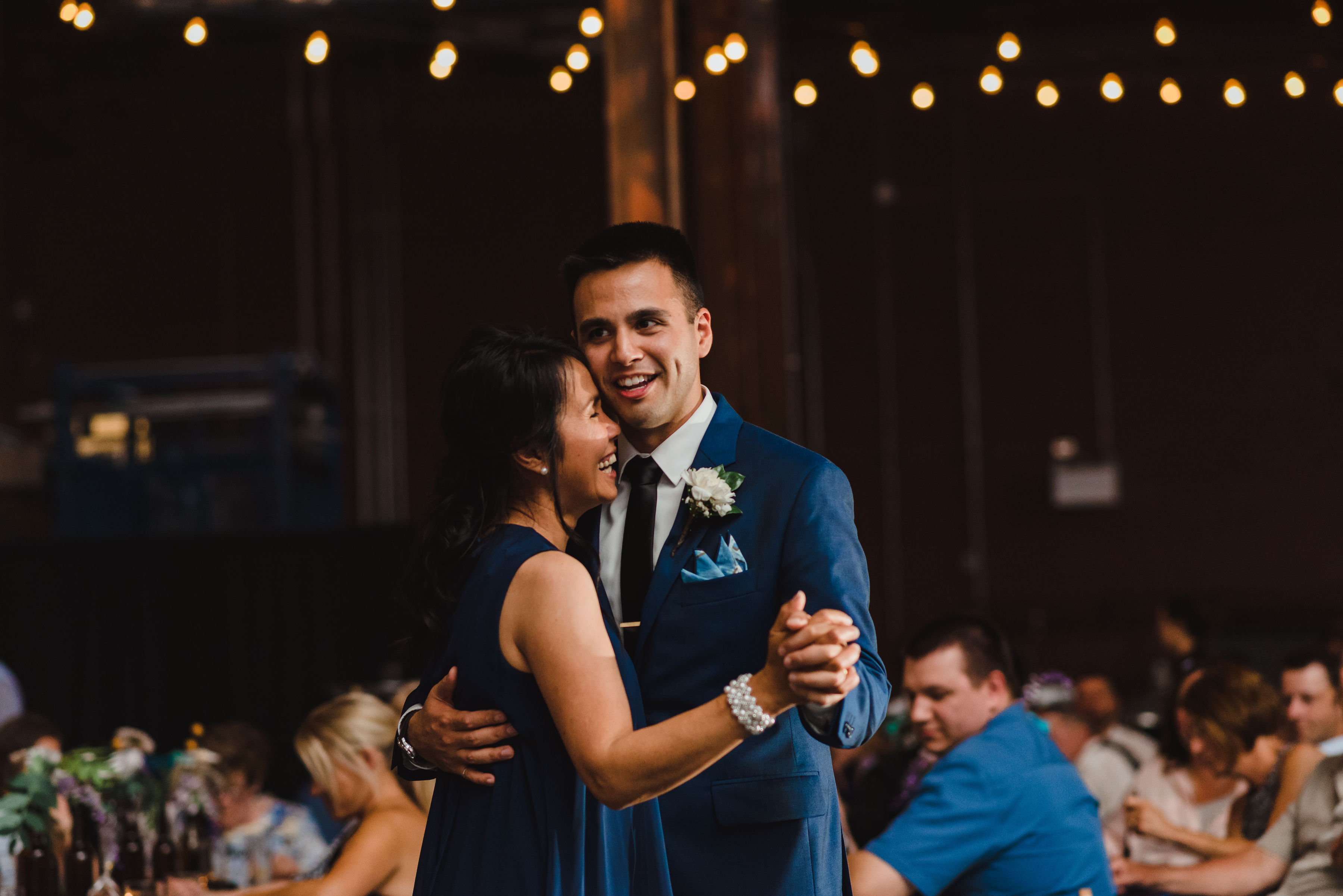 wedding guests watch from tables as groom and his mother share a dance Junction Craft Brewing wedding photography