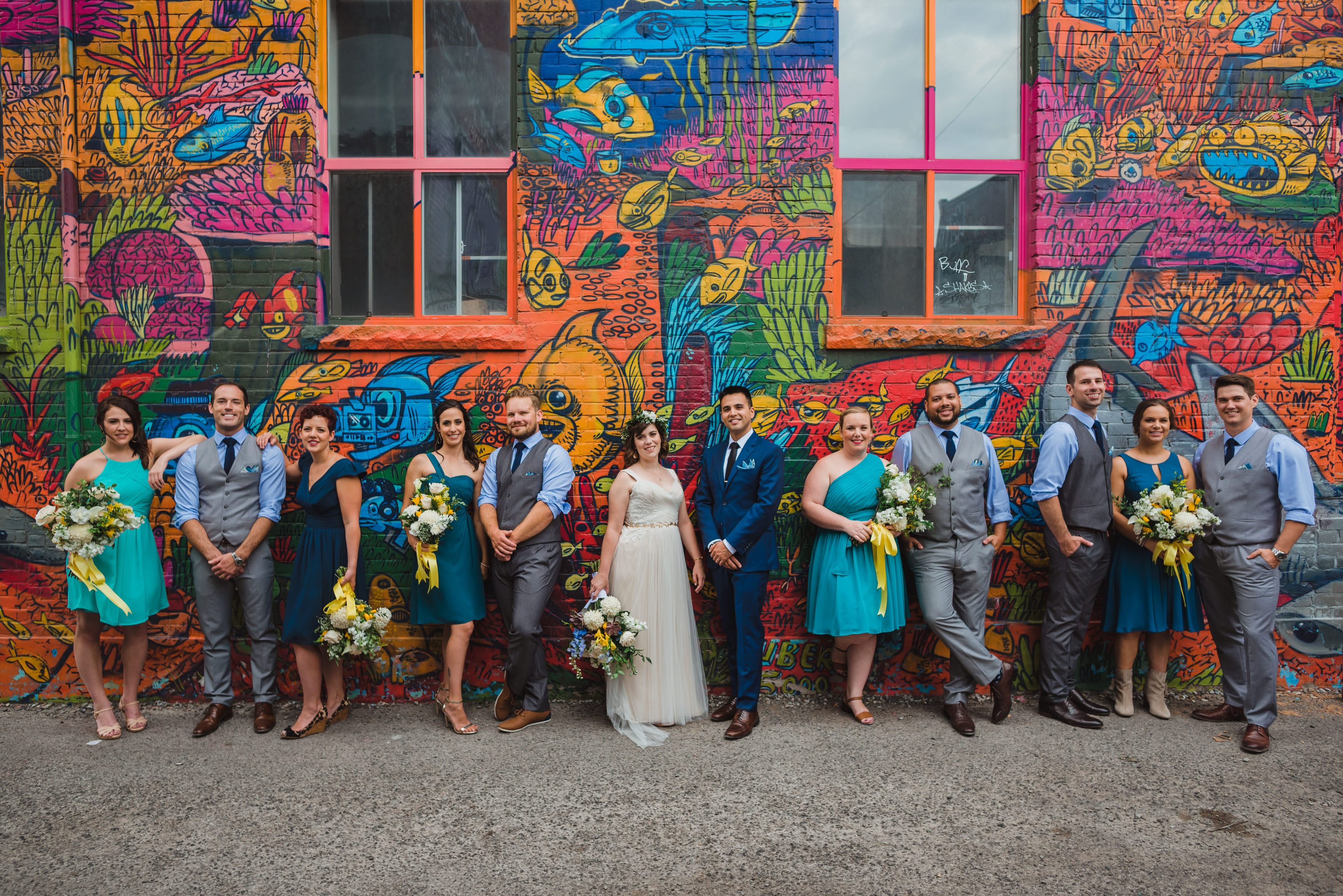 bride and groom leaning up against a graffitied wall with their wedding party Toronto Junction Craft Brewing wedding