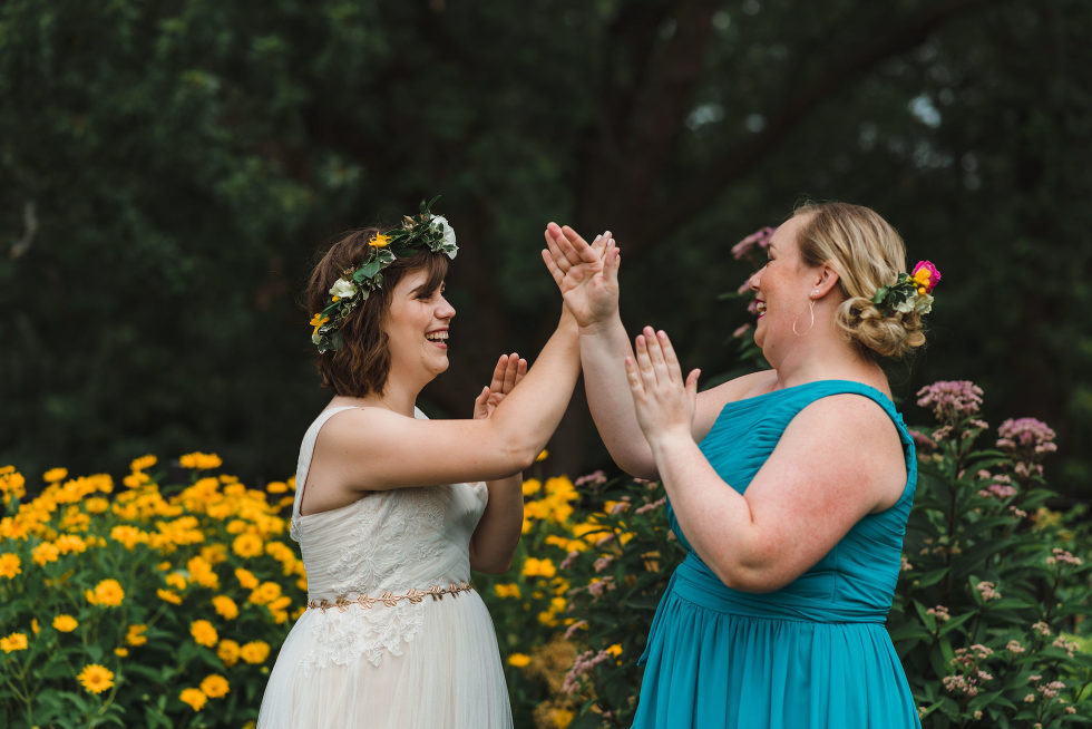 bride and her bridesmaid in a garden playing patty cake Toronto Junction Craft Brewing wedding photography