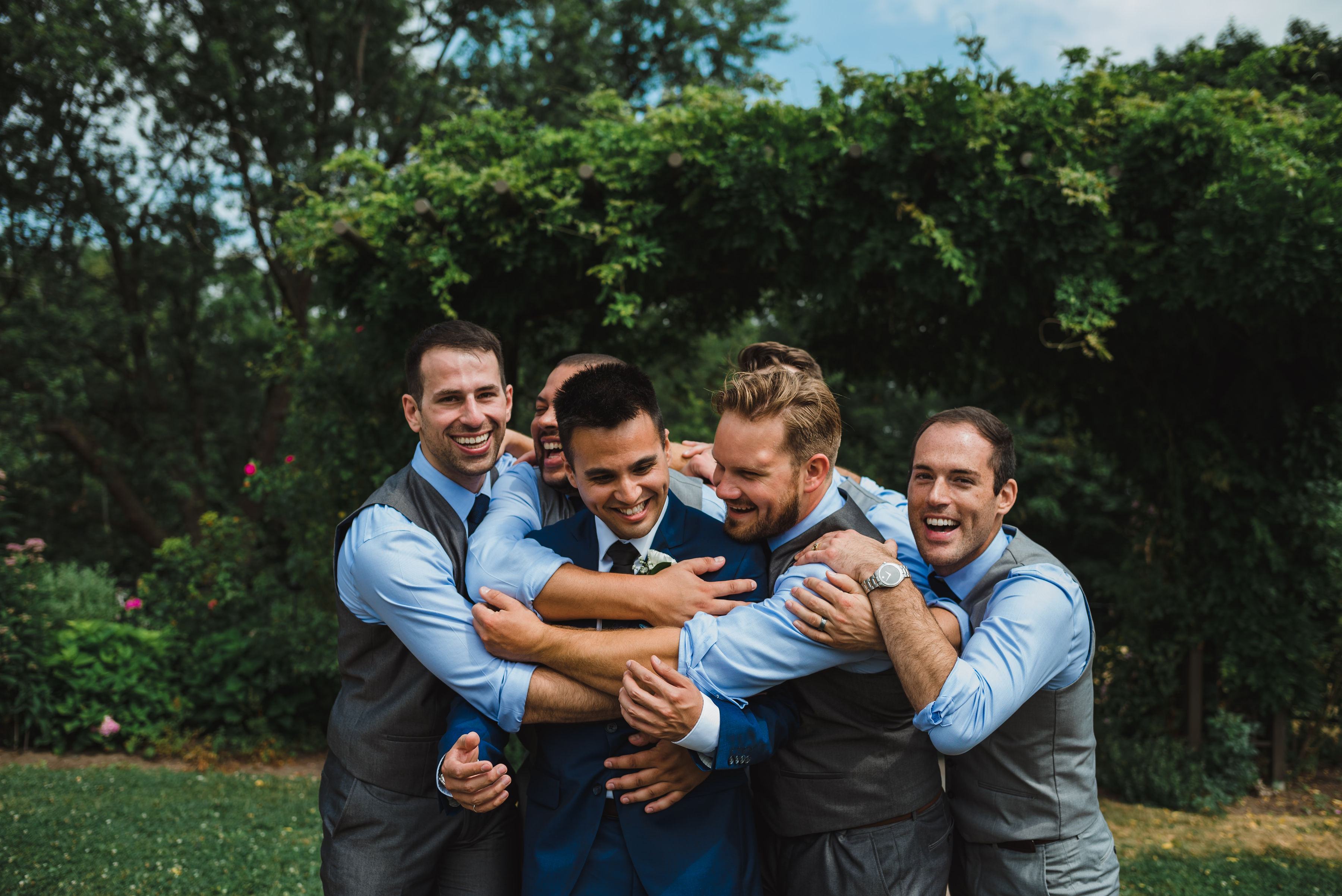 groom smiling as his groomsmen all wrap their arms around him in a park Toronto Junction Craft Brewing wedding
