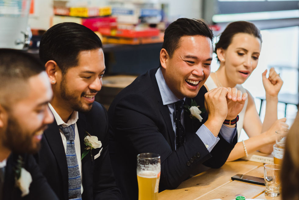 bride, groom, and wedding guests crowded around a picnic table with pints of beer at Henderson