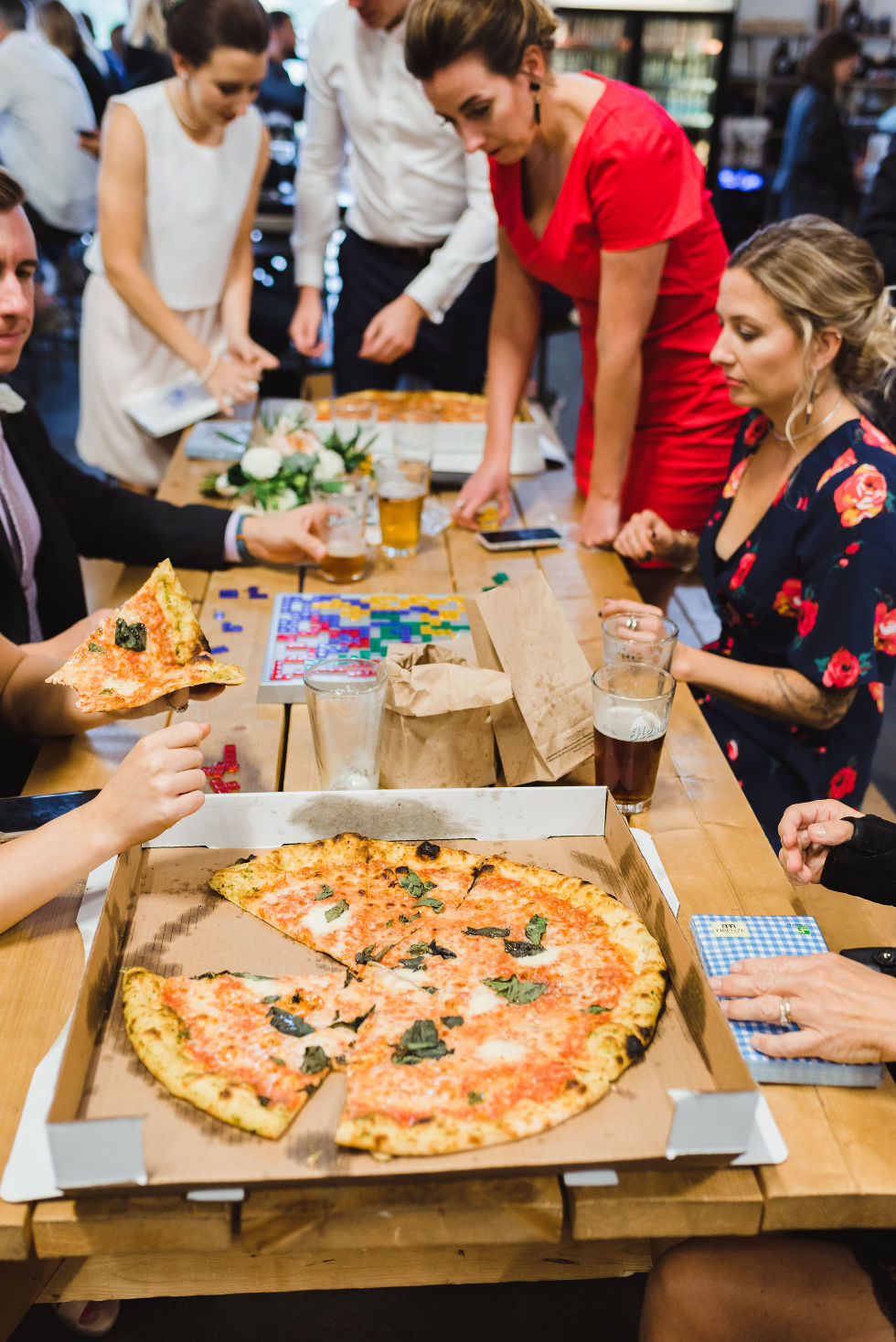 wedding guests sitting at picnic tables playing games and drinking pints of beer and eating pizza at Henderson
