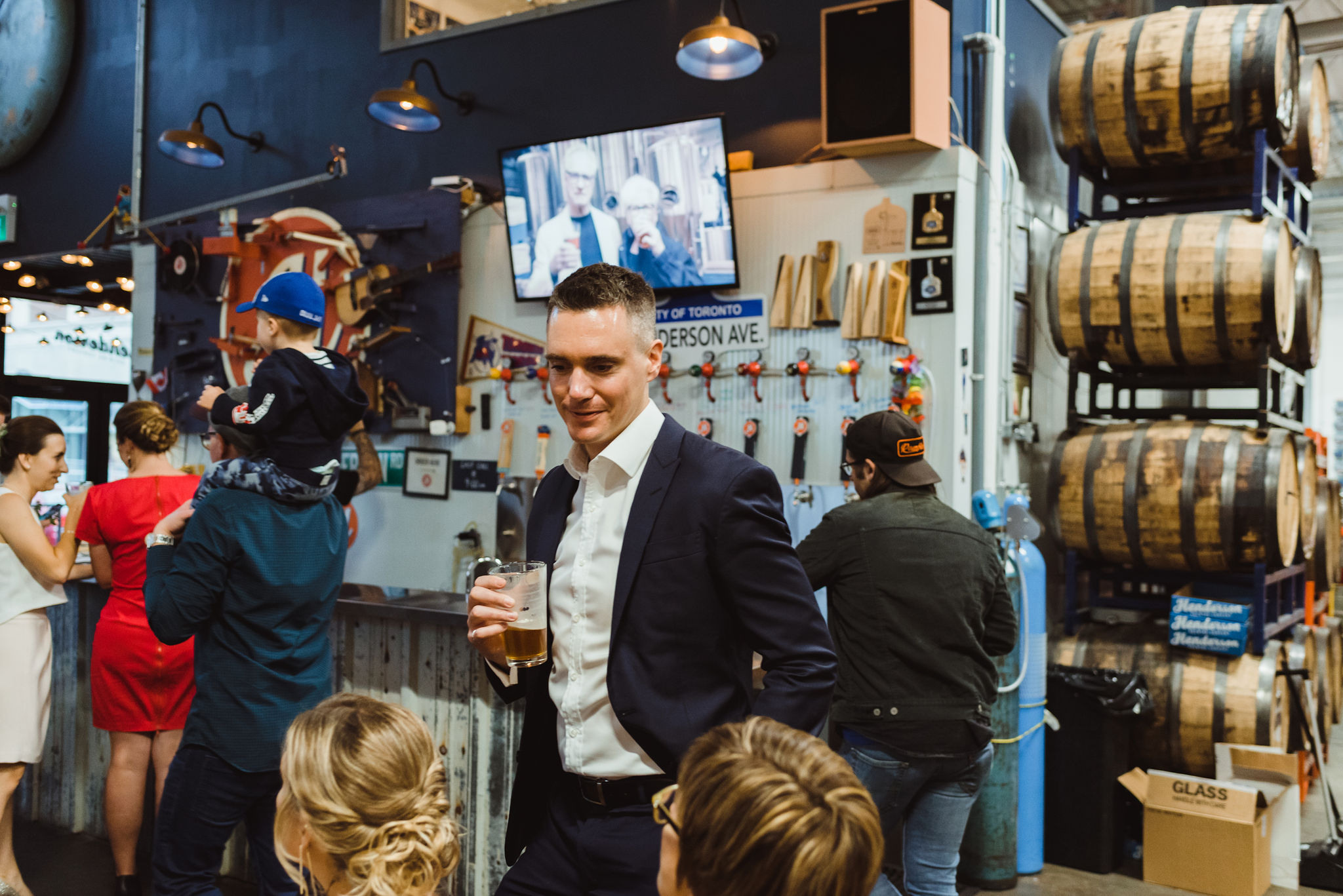 wedding guests holding pints with wooden barrels and taps behind them Henderson's Brewing Company Toronto wedding photography how to best plan your wonderful wedding your way 