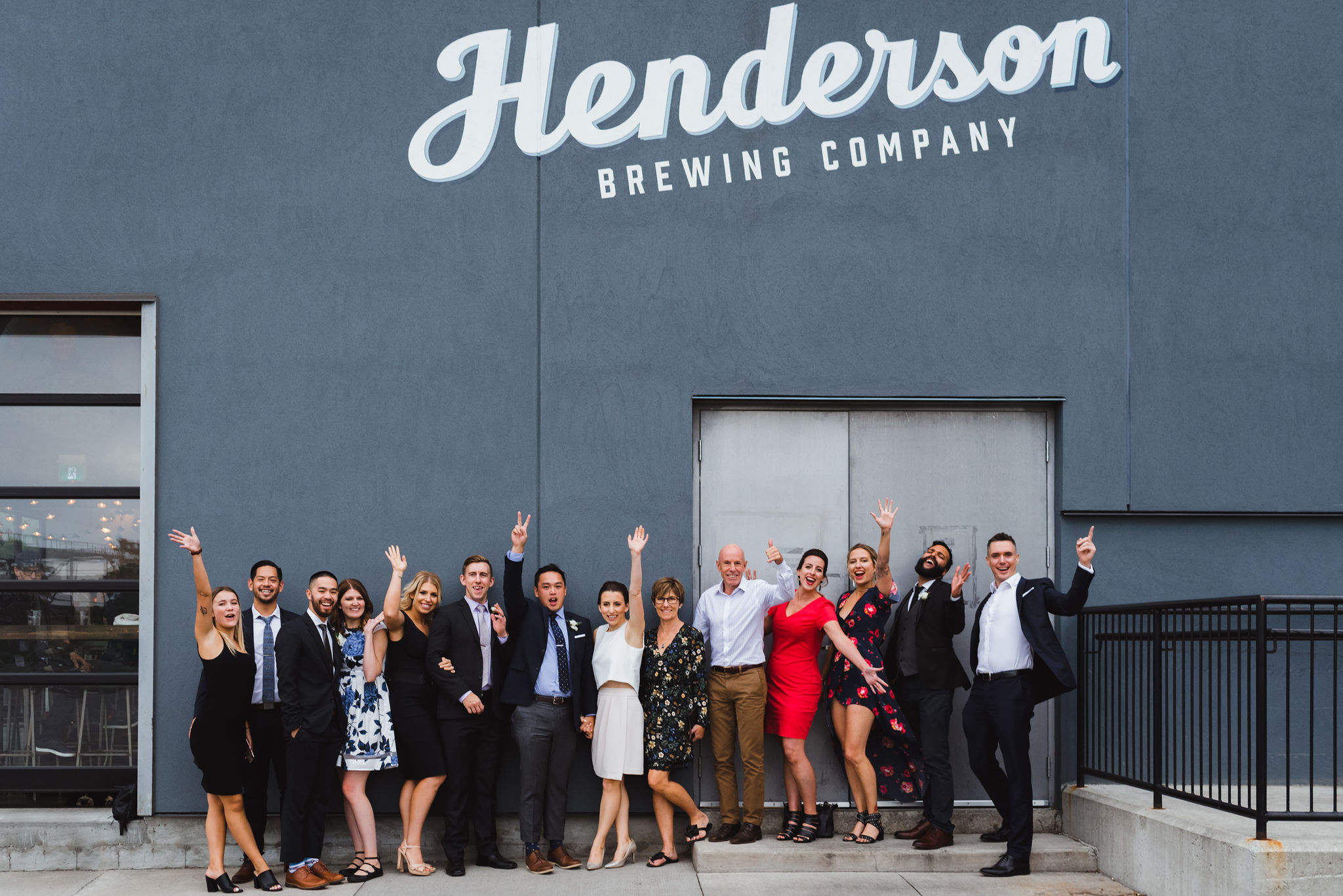 wedding guests with their arms in the air standing out front of the Henderson Brewing Company building Toronto wedding photography