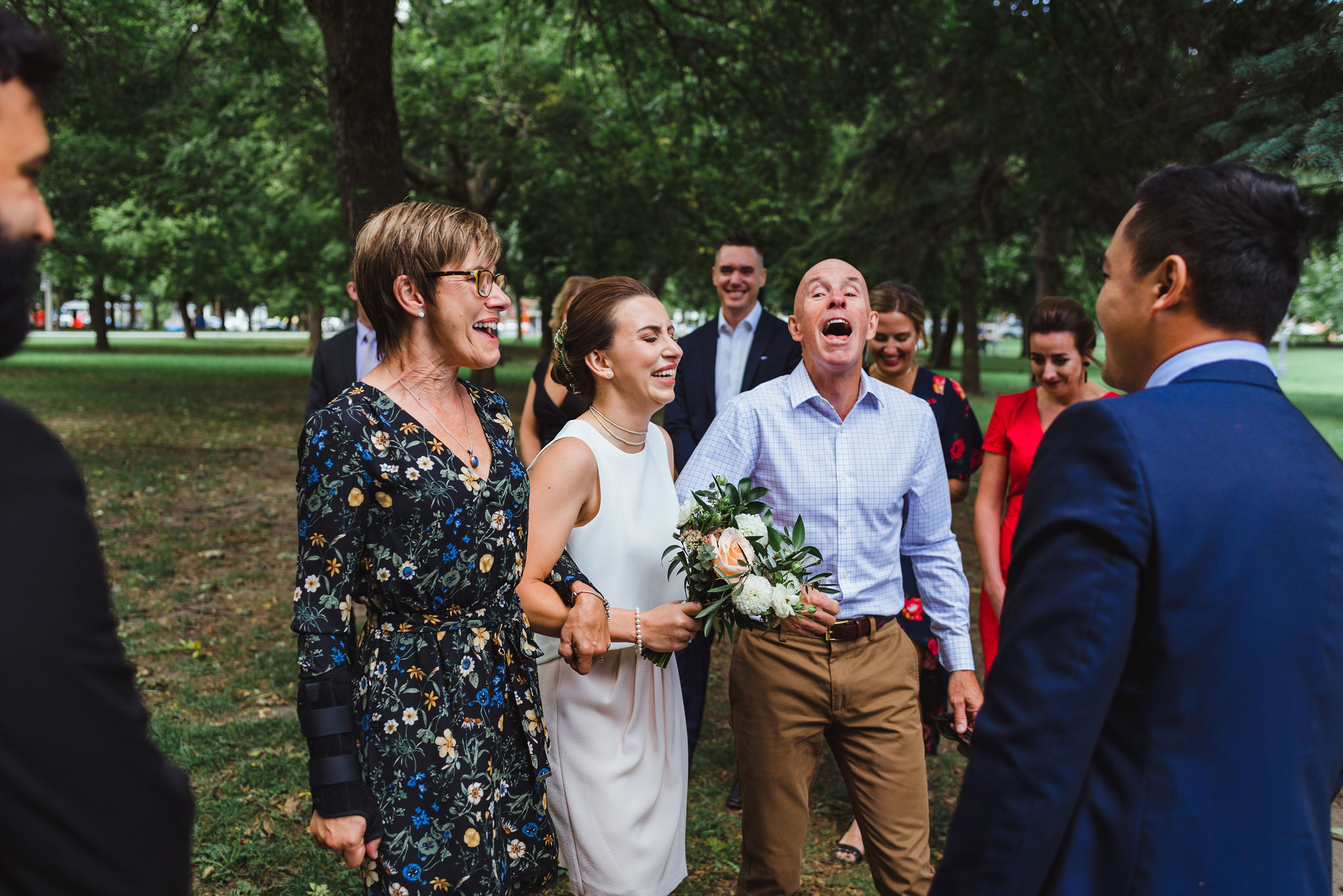 bride and her parents laughing while they are escorting her down the aisle to the ceremony in Trinity Bellwoods Park Toronto Canada