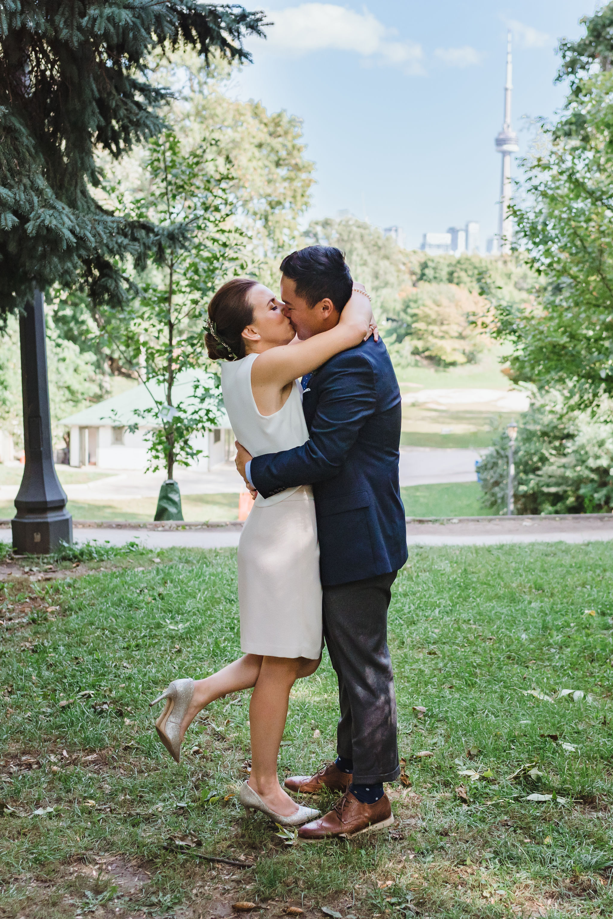 bride and groom kissing after wedding ceremony in Trinity Bellwoods Park with view of CN tower Toronto