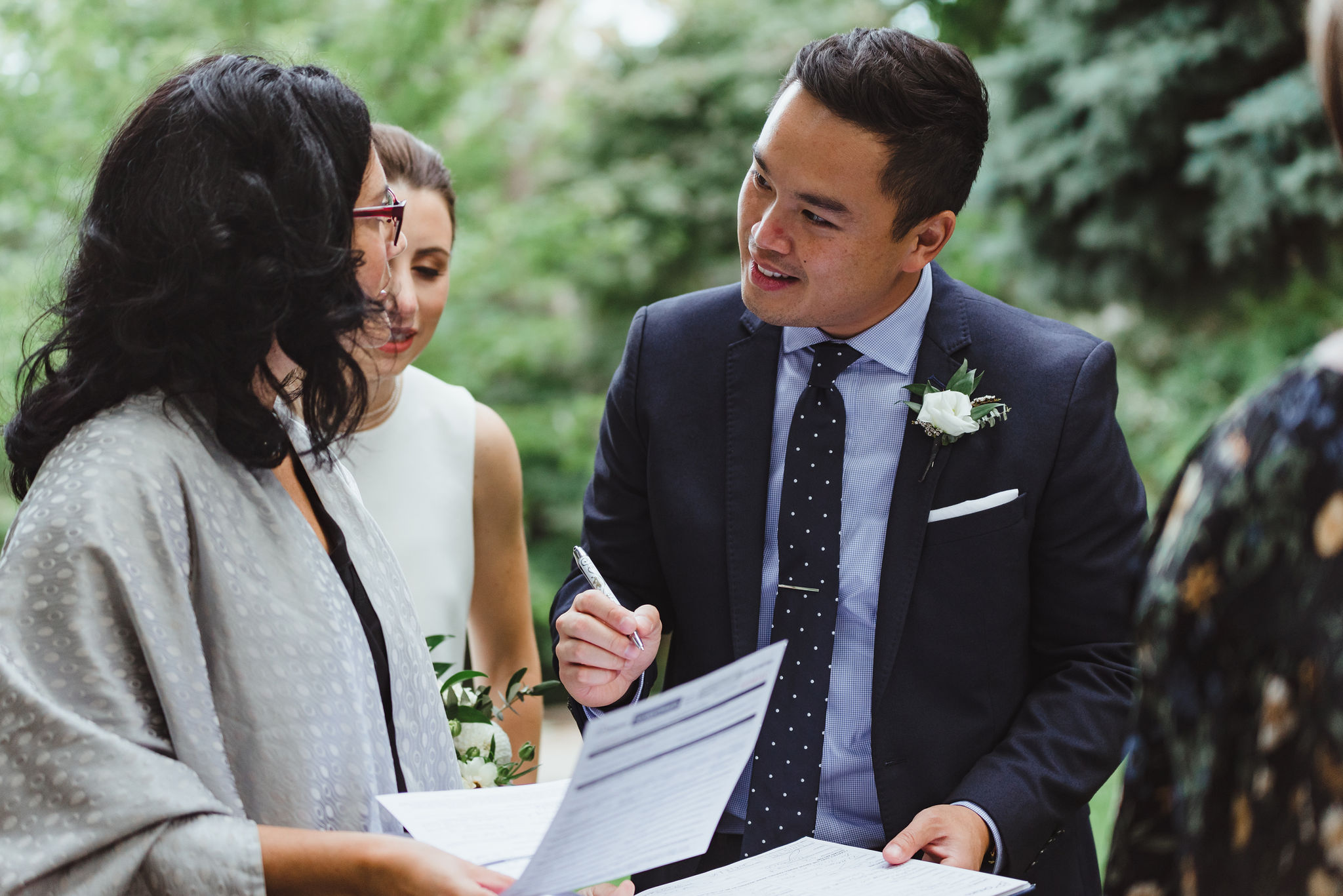 groom signing wedding certificate as bride and officiant look on Trinity Bellwoods Park Toronto