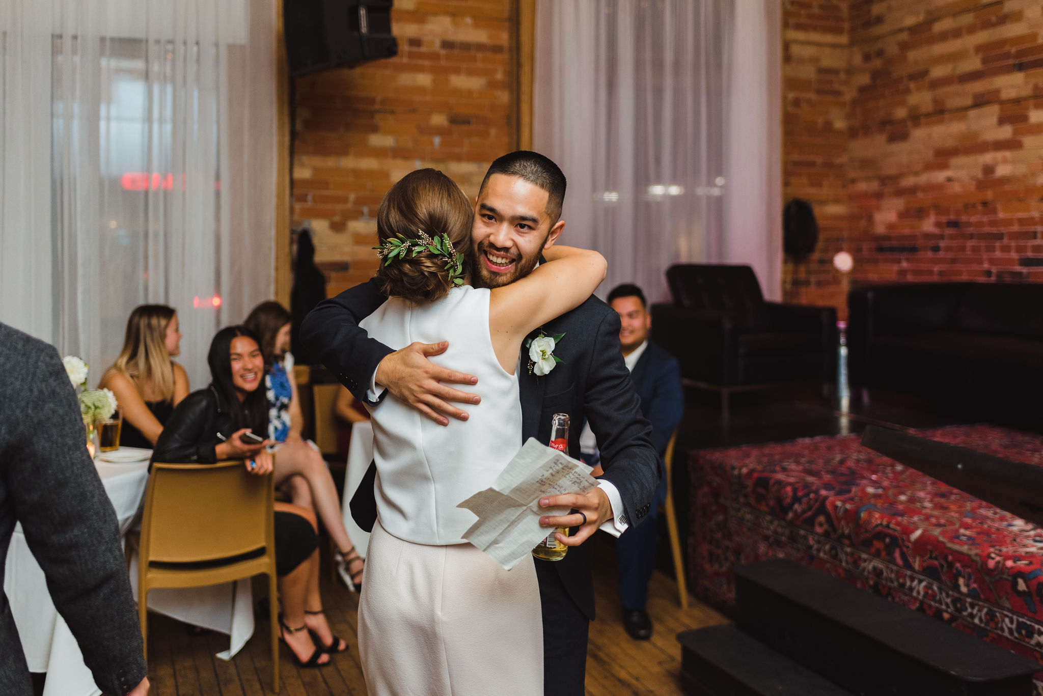 groomsman hugging the bride holding a beer and piece of paper during the wedding reception at the Gladstone Hotel in Toronto