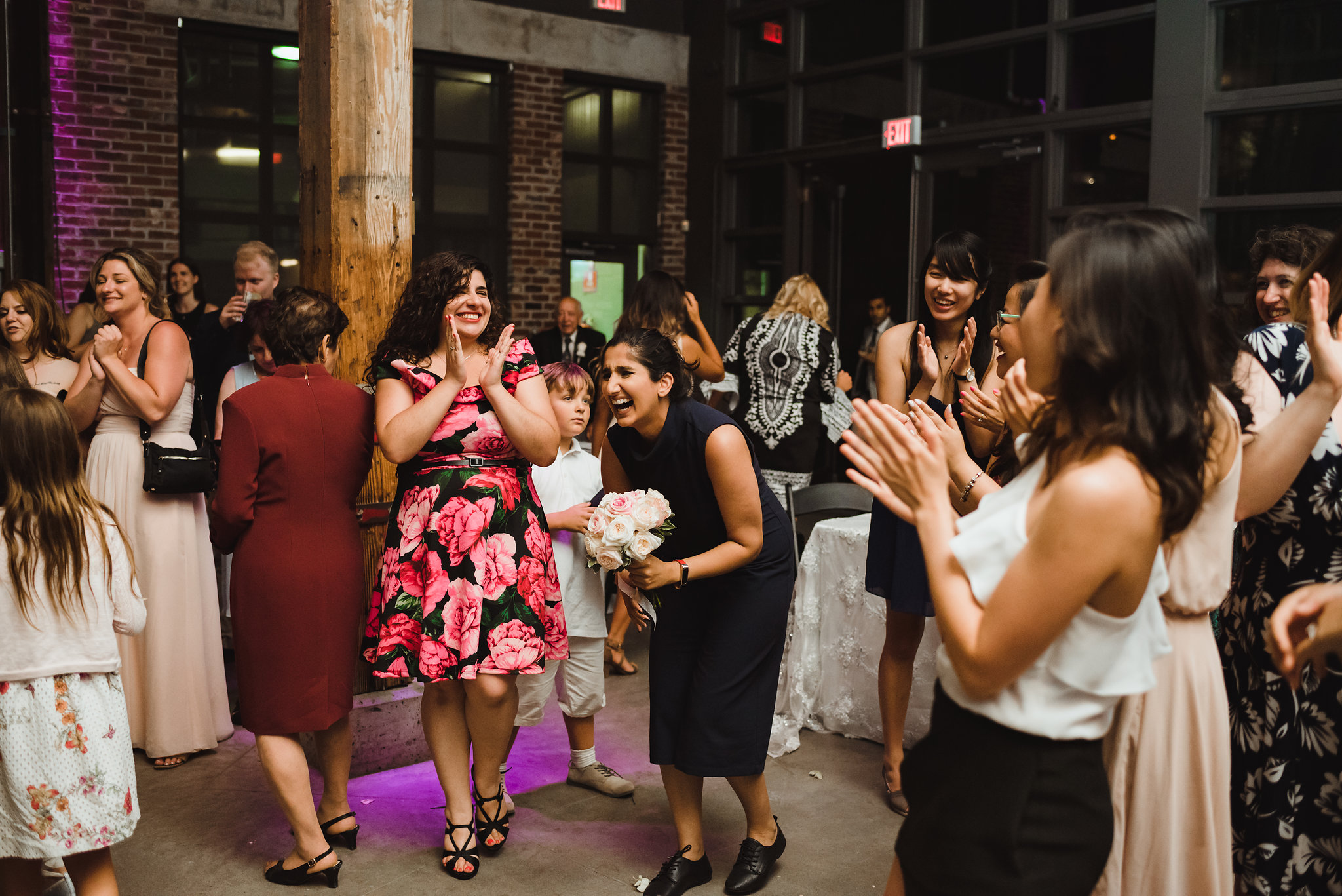 woman laughing as she caught the wedding bouquet as other wedding guests clap around her Steam Whistle Brewing Toronto wedding photography woman laughing as she caught the wedding bouquet as other wedding guests clap around her Steam Whistle Brewing Toronto wedding photography