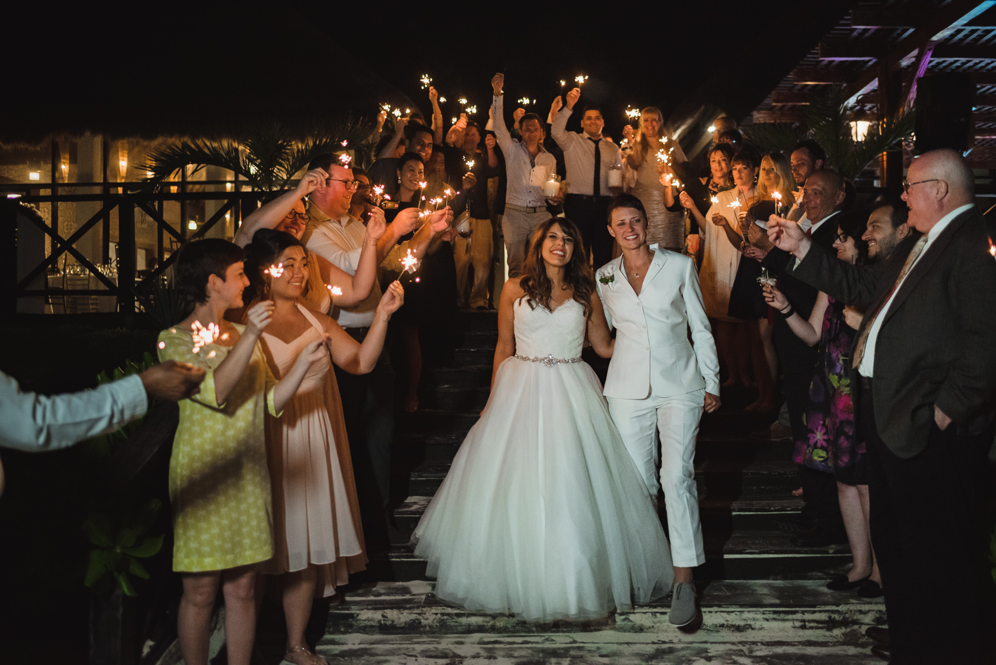 brides exiting wedding reception with wedding guests surrounding them and holding sparklers at Now Sapphire Resort in Mexico