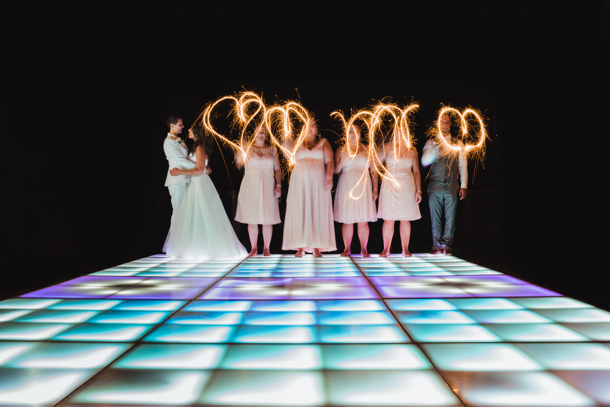 brides slow dancing on multi-coloured light up dance floor next to wedding party using sparklers to draw hearts in the air Now Sapphire Resort Mexico 