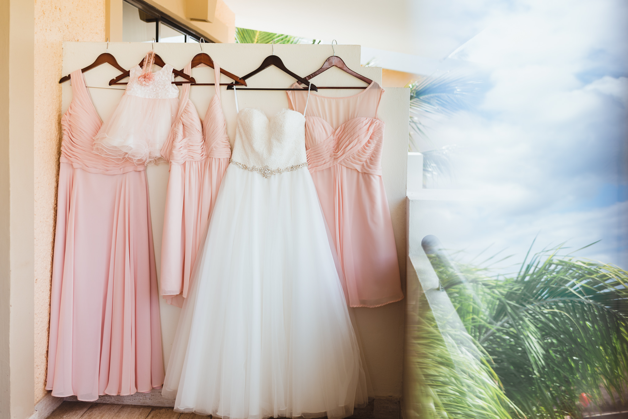 white brides dress and pink bridesmaids dresses hung on hangers before destination wedding at Now Sapphire Resort in Mexico 