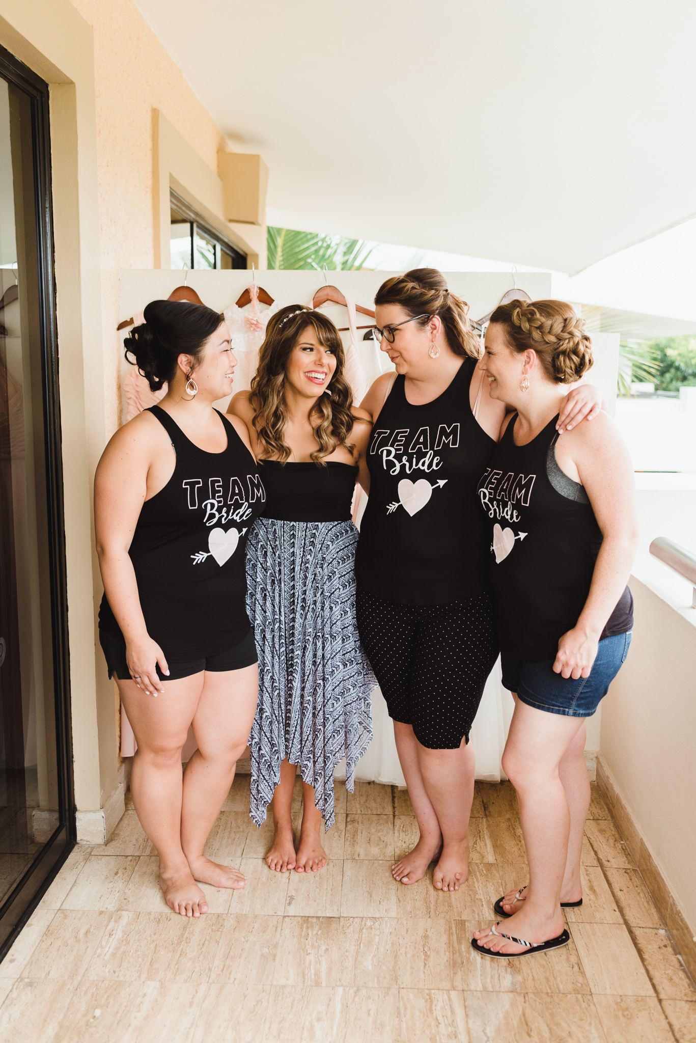 bride surrounded by bridesmaids wearing "Team Bride" black tank tops before destination wedding at Now Sapphire Resort in Mexico